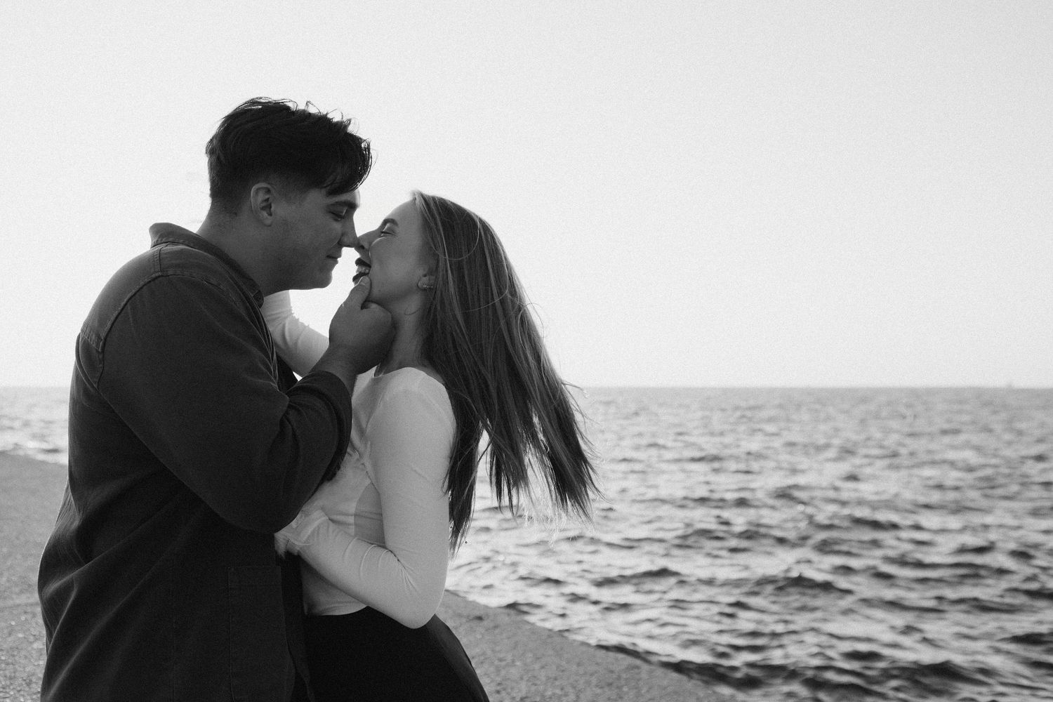 A romantic black and white photo series of a couple embracing on a beach at sunset.