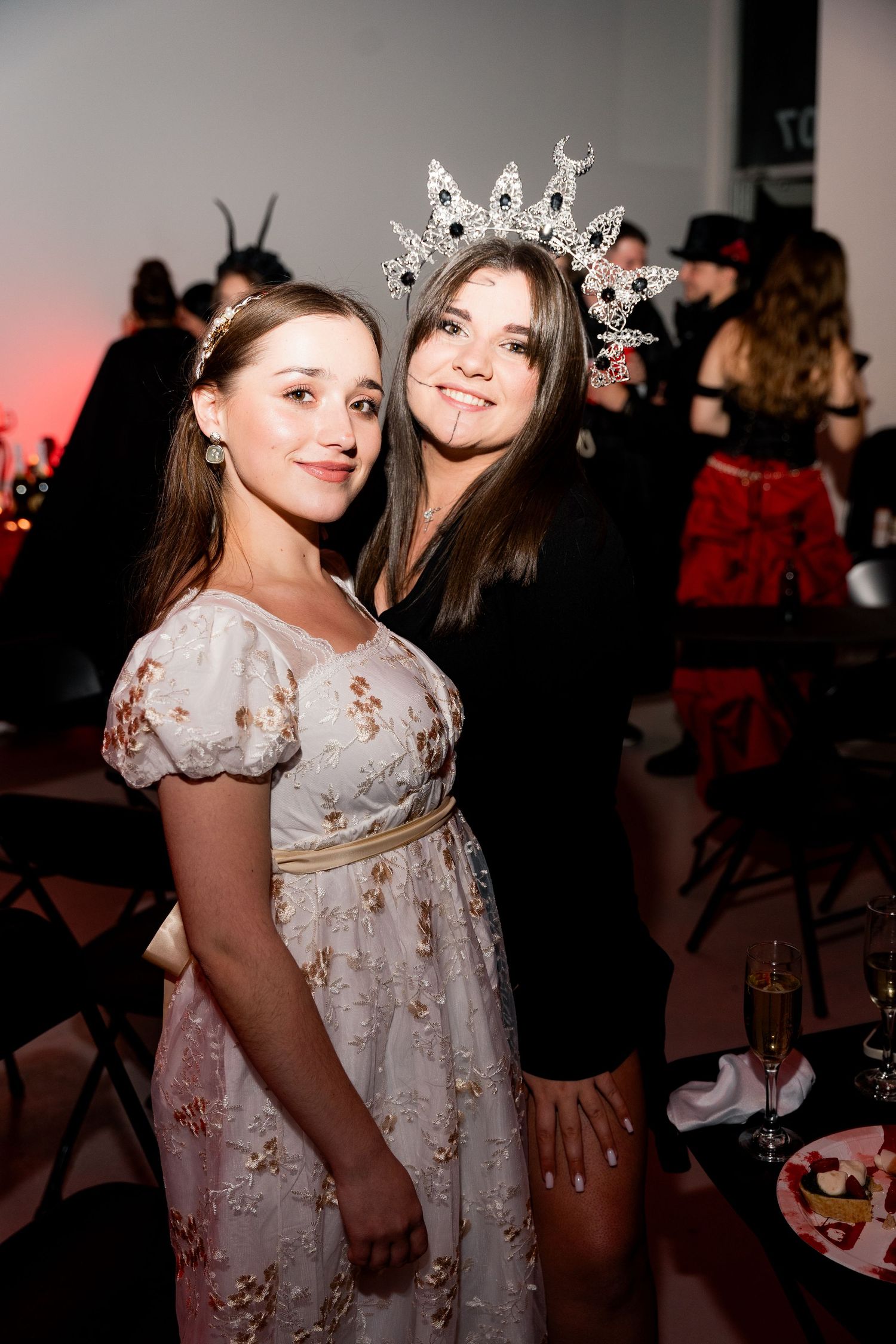 Two people pose at a costume party, one wearing a princess dress and crown.