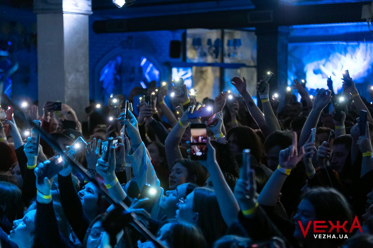 Concert crowd holds up illuminated phones creating sea of lights during performance.