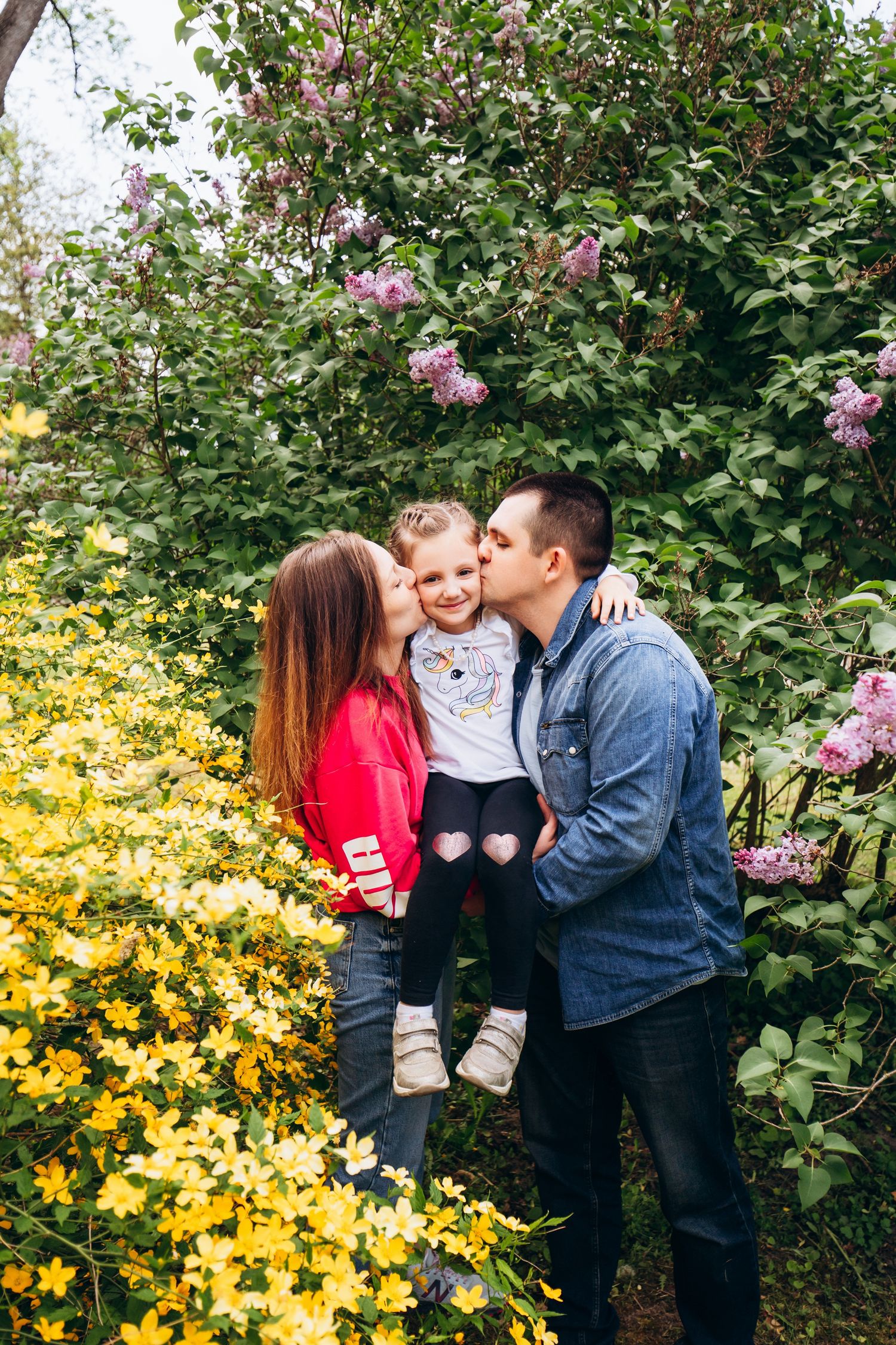 A sweet family moment in a garden with pink lilac blooms and yellow flowers in the background.