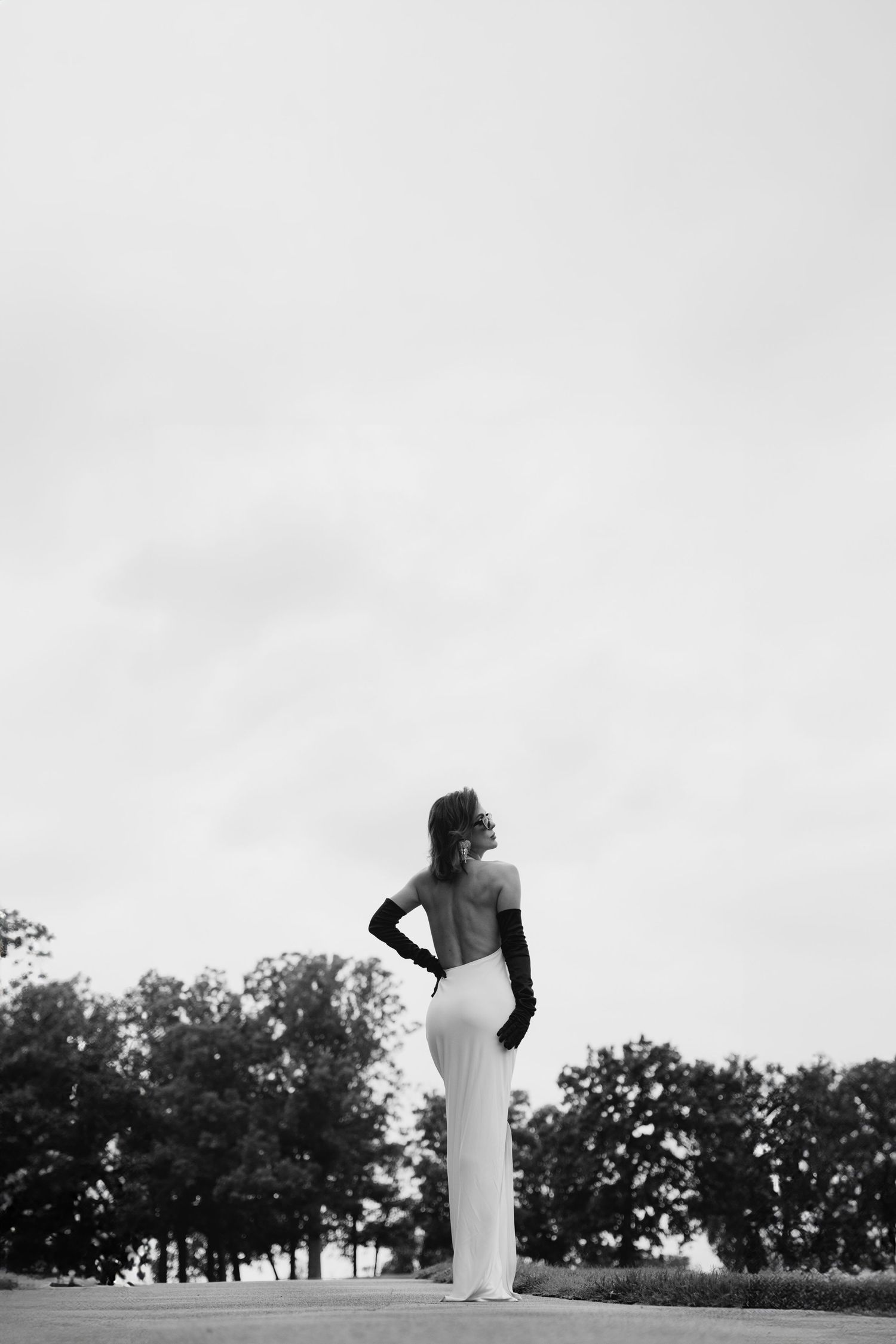 Black and white silhouette of person in flowing gown standing against cloudy sky.