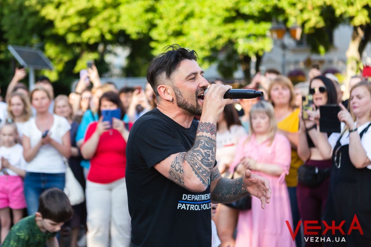 Performer singing into microphone at outdoor concert with enthusiastic audience.