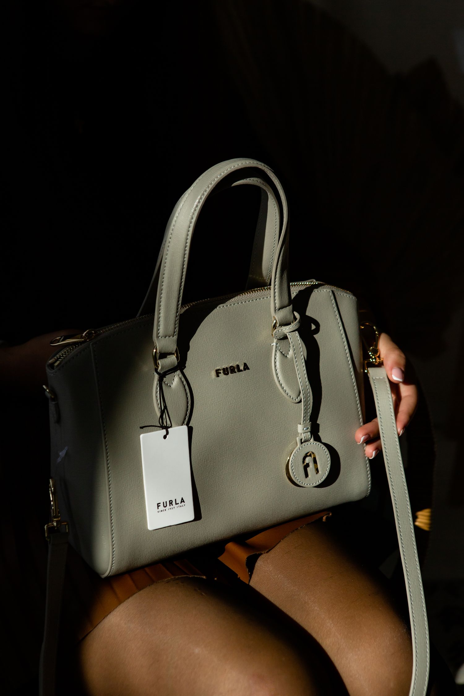 Grey Furla handbag with shoulder strap photographed in dramatic lighting.