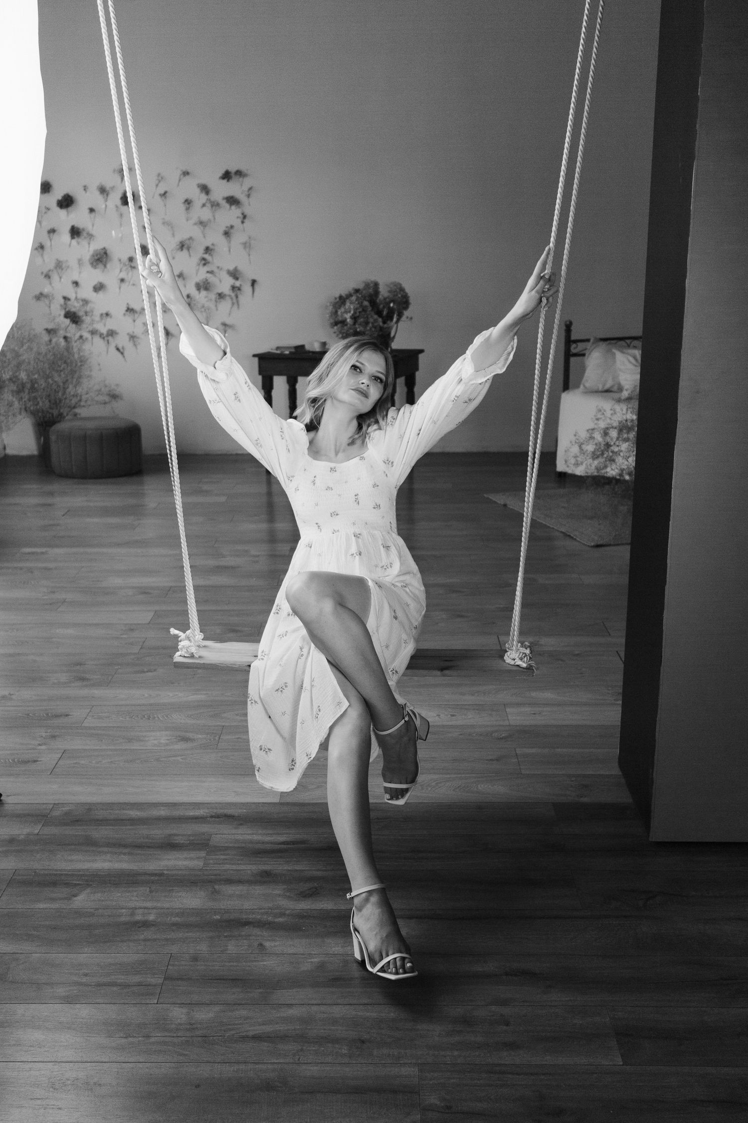 Black and white photo of joyful moment on indoor rope swing wearing floral dress.