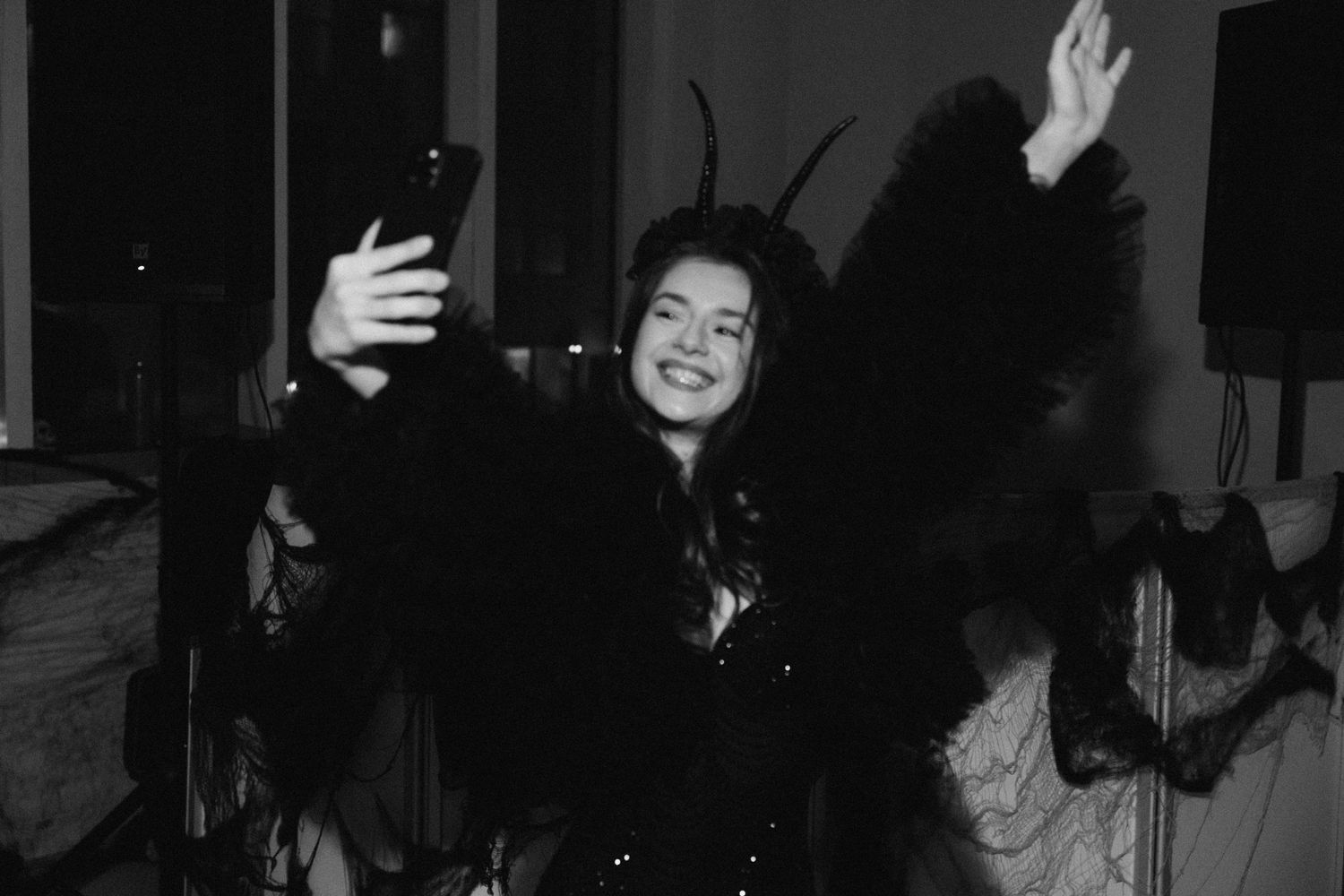 Person in dark costume takes a selfie while dancing at a party.