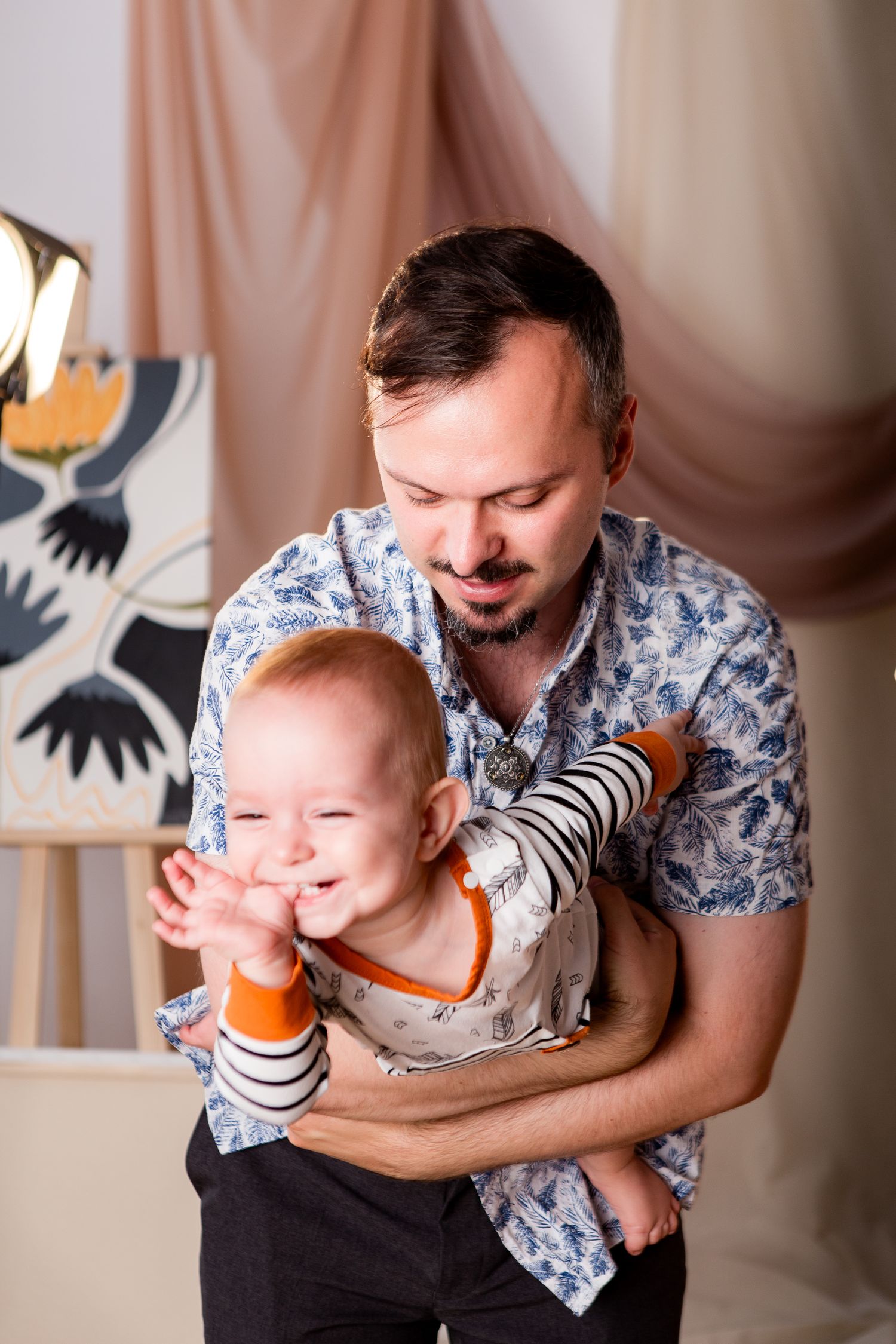 A tender moment shared with a laughing baby in a striped outfit against a fabric backdrop.