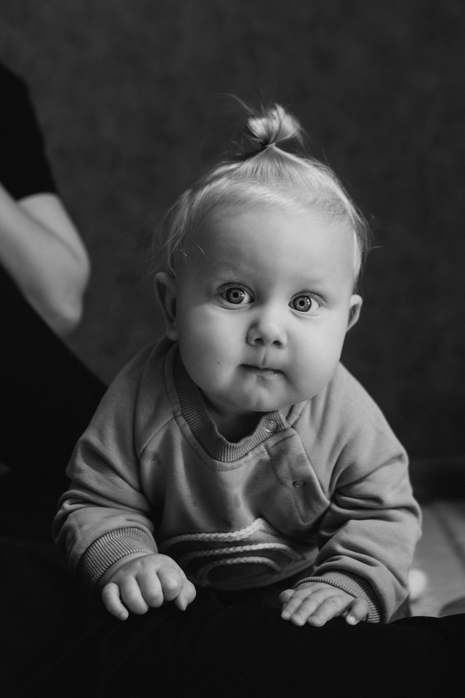 A series of black and white photos showing a baby lying on their stomach in a sweater with various sweet expressions.