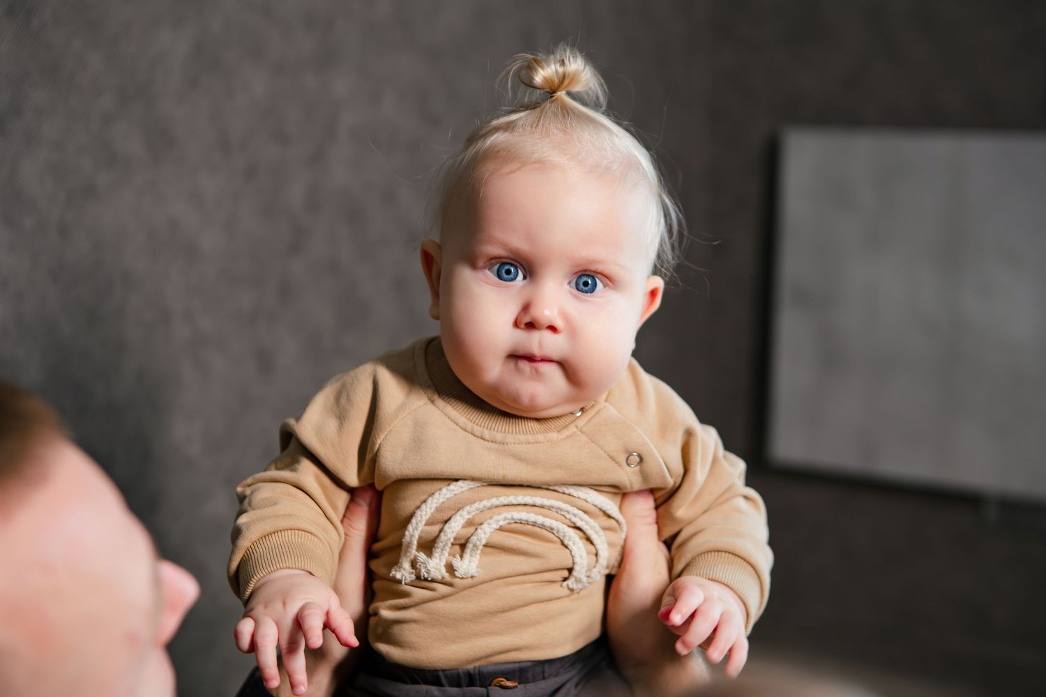 A baby in a tan onesie is shown in a series of connected photos against a dark background.