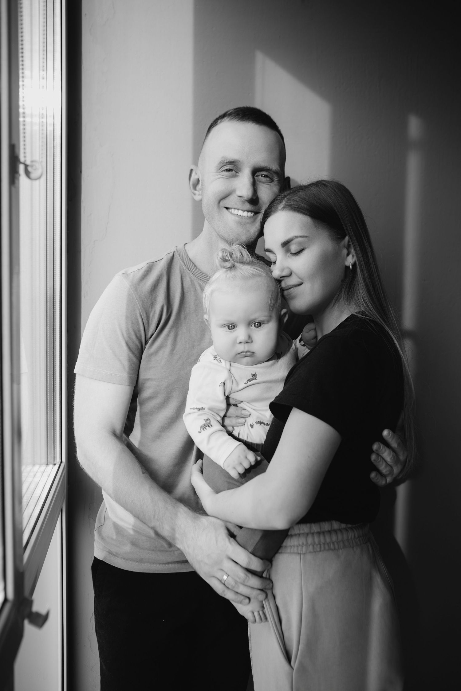 A black and white photo series shows tender moments between parents and their baby in an intimate home setting.