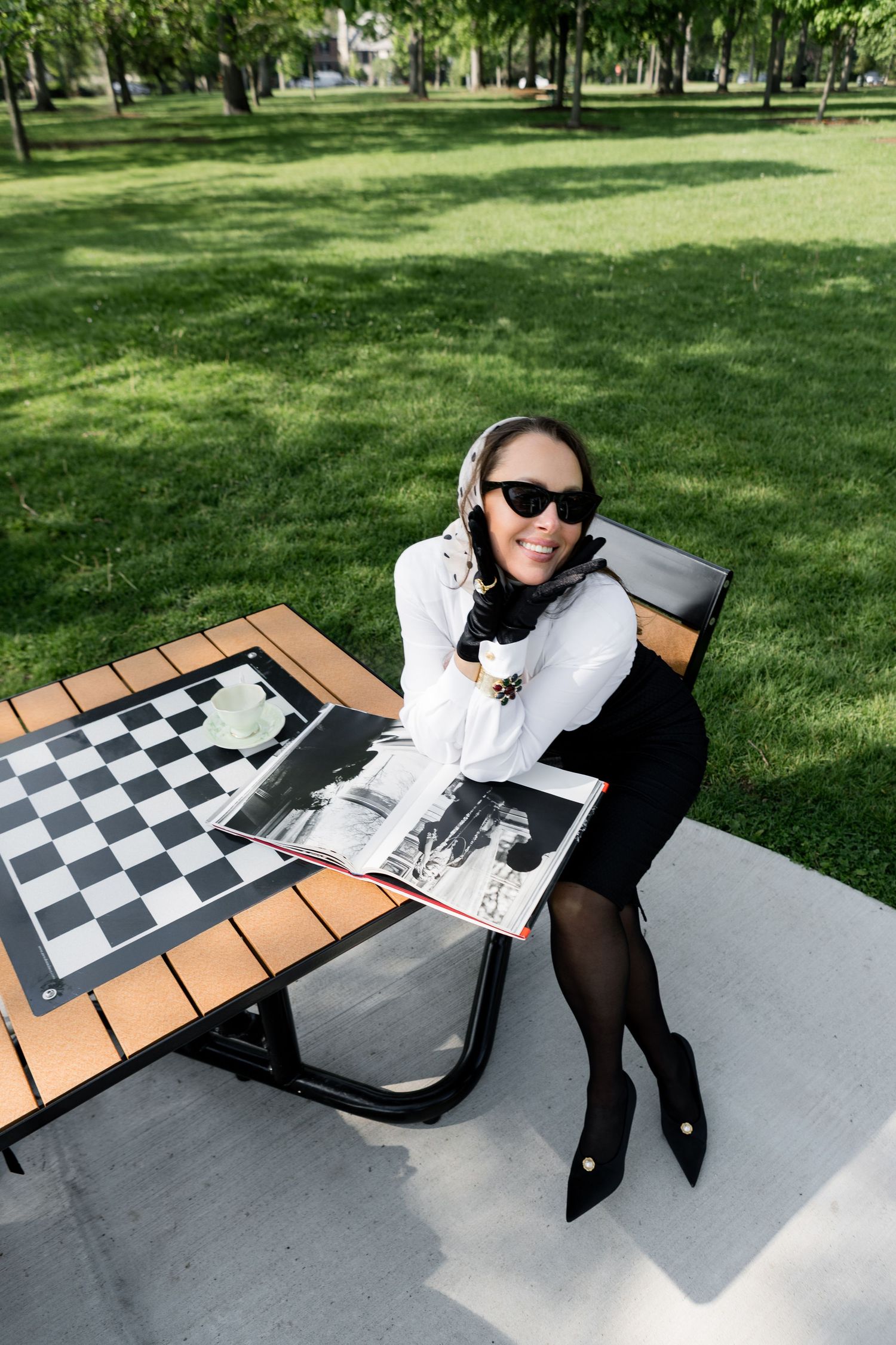 A person relaxes on a picnic blanket with a chess board in a sunny park setting.