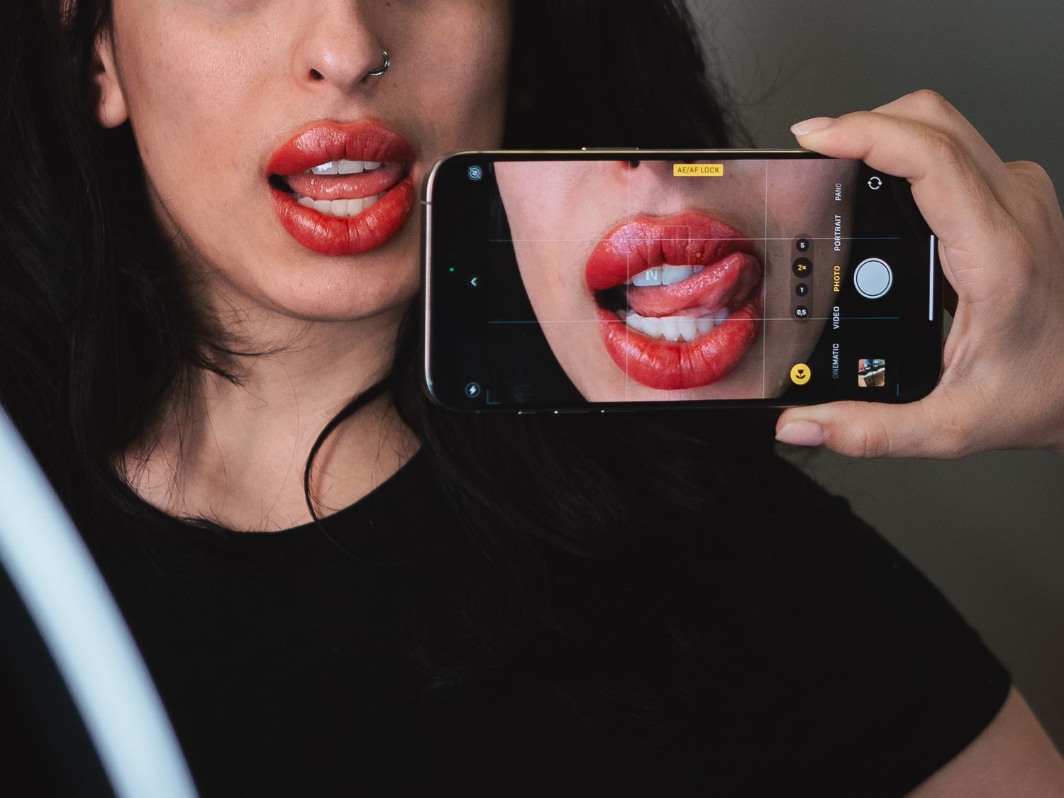 Person taking selfie of red lipstick with smartphone camera.