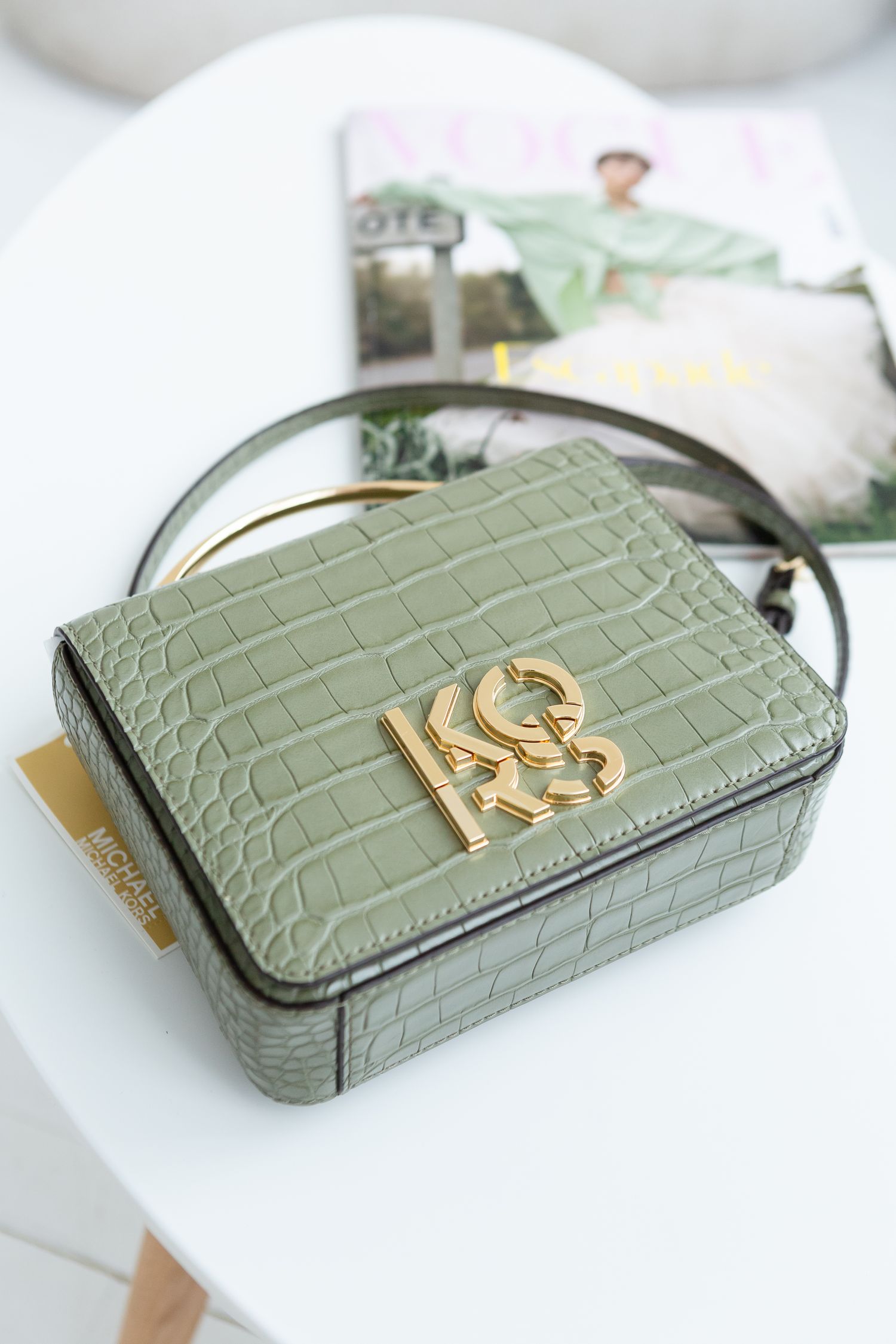 Sage green crocodile-embossed Michael Kors crossbody bag with gold hardware on white surface.