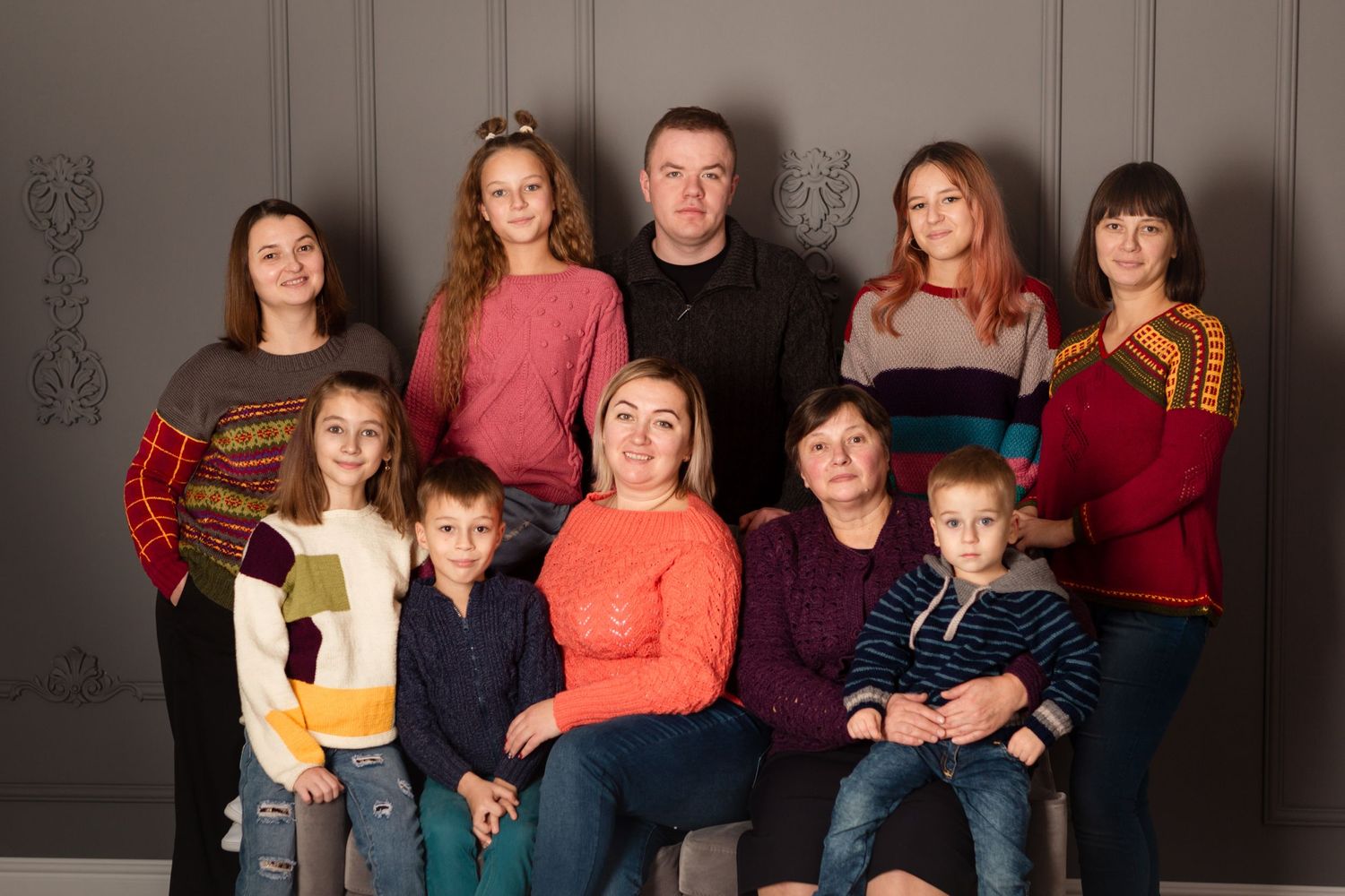 Family group photo with colorful sweaters and traditional elements against neutral backdrop.