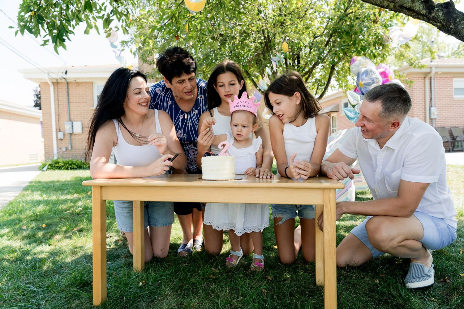 A joyful outdoor celebration with people gathered around a wooden table under trees.