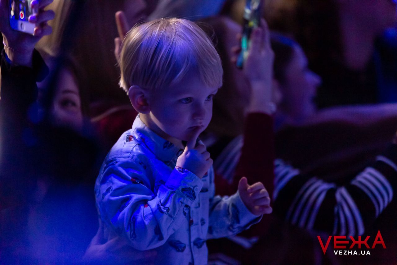 A young child in blue dances at a concert with dramatic lighting.
