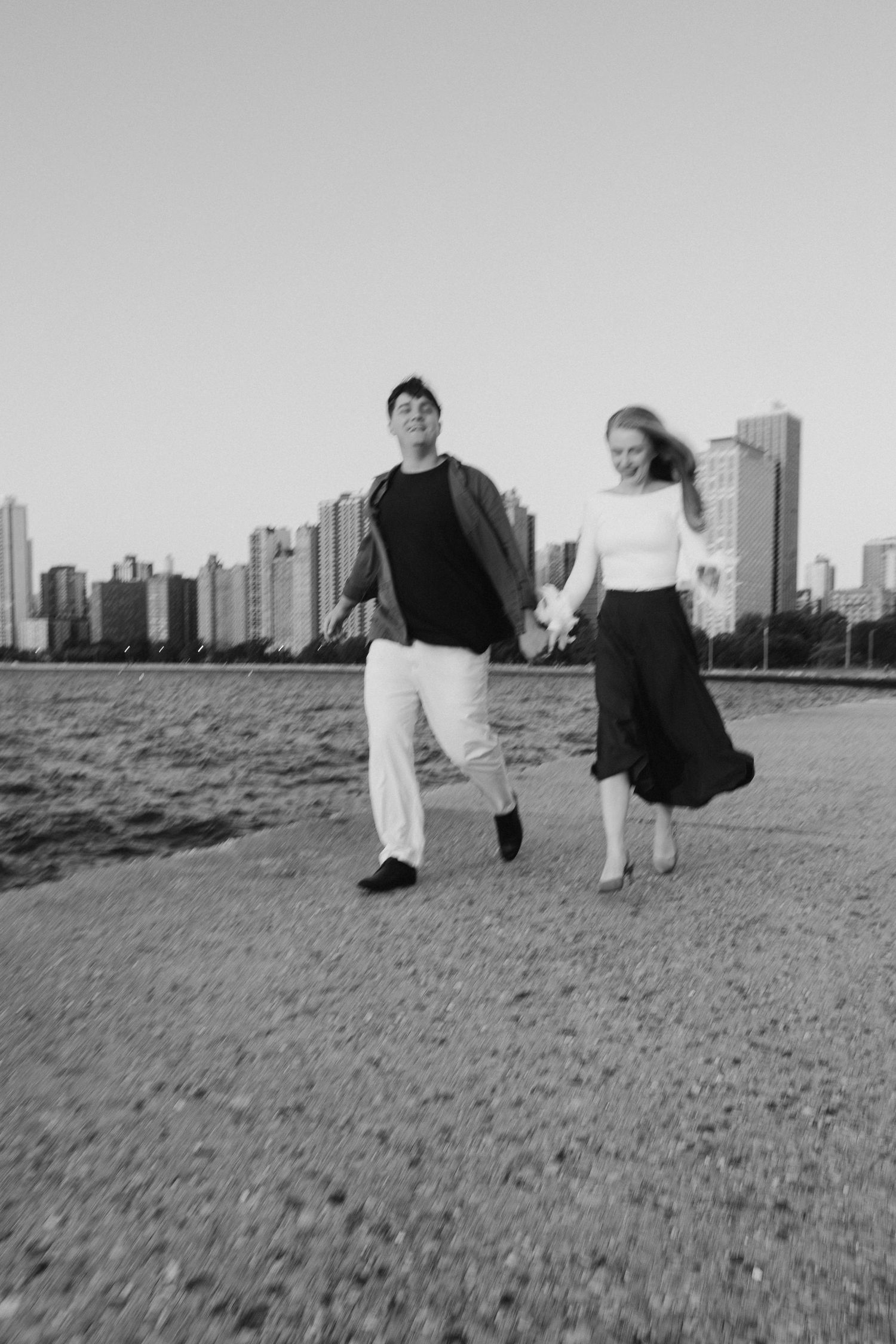 Three figures walk together across a grassy field with a city skyline visible in the background.