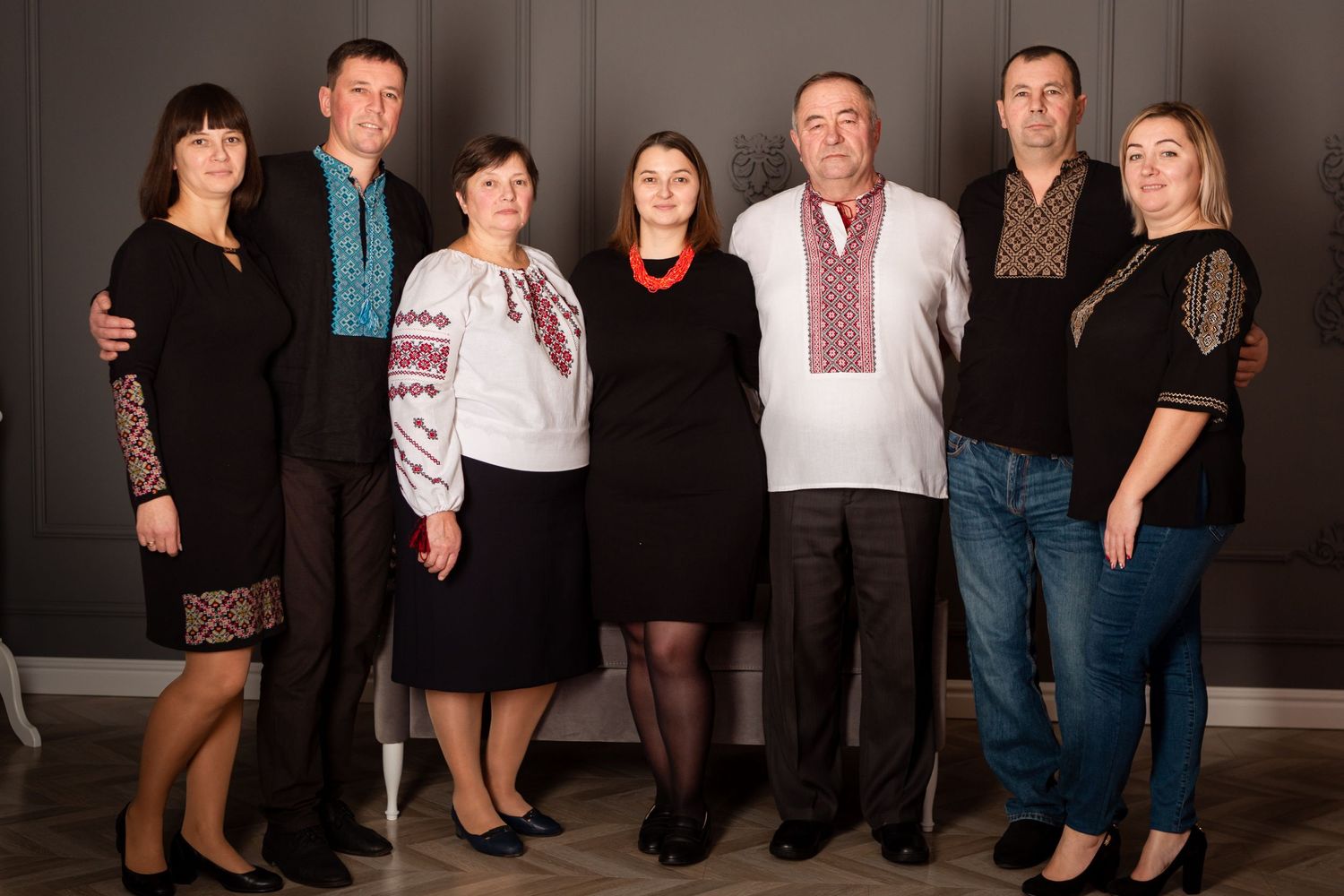 Multi-generational family portrait with members wearing traditional embroidered shirts against dark background.
