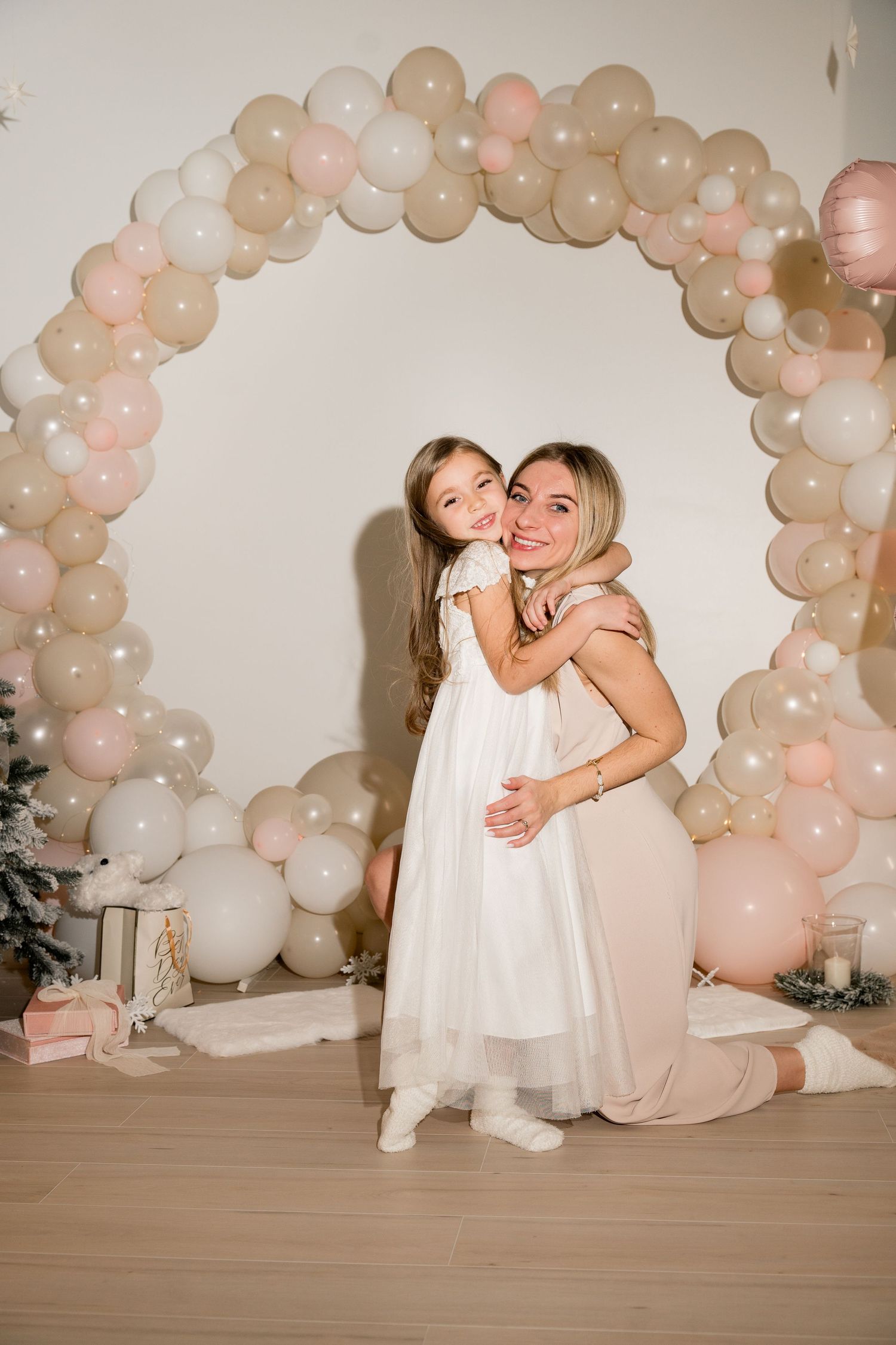 Sweet moment captured under a pastel balloon arch with matching neutral outfits.