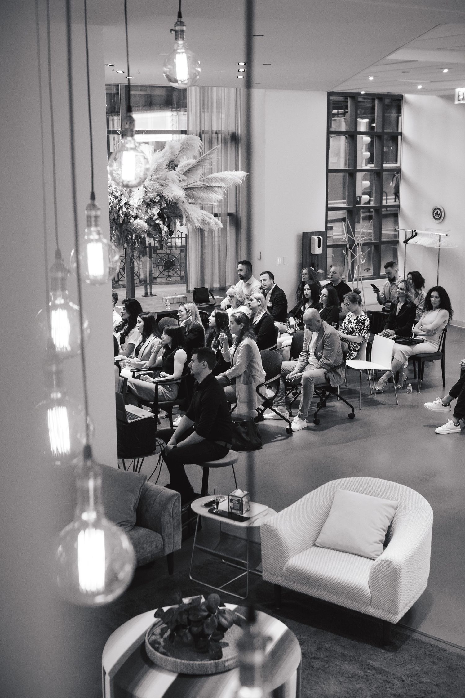 Black and white photo of an audience seated at a corporate event with hanging pendant lights.