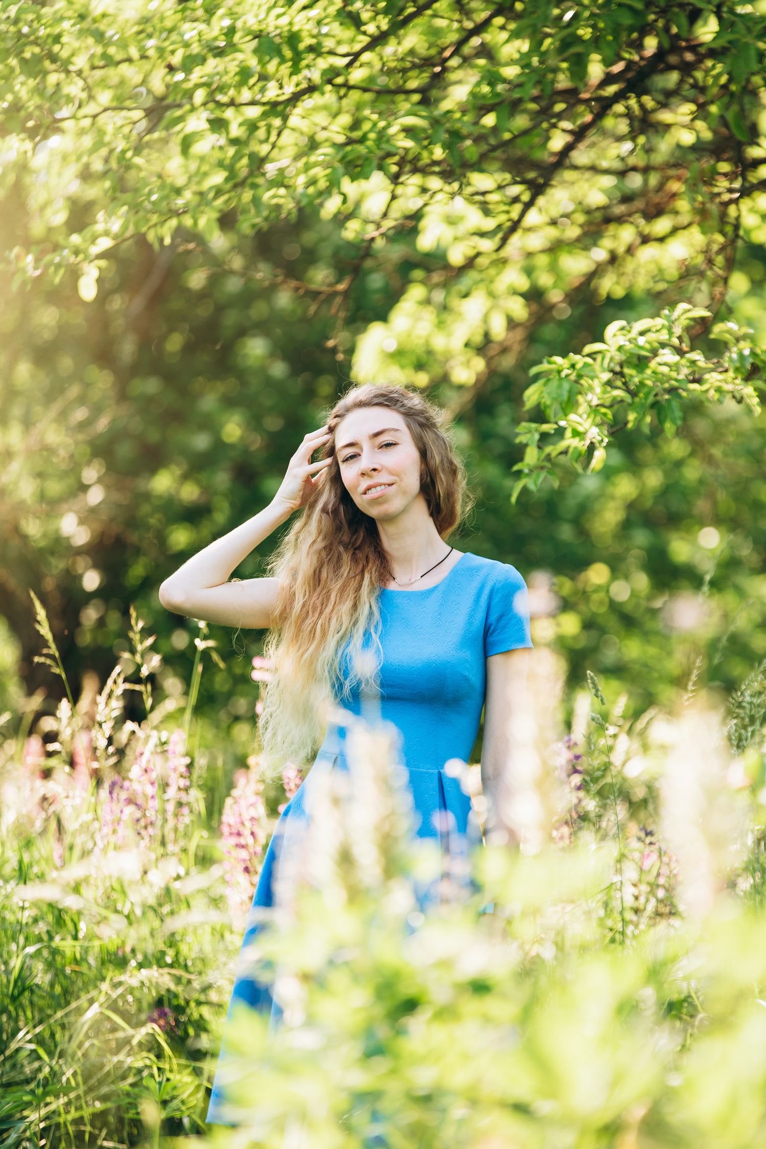 Woman in blue dress enjoying summer day among wildflowers and green foliage.