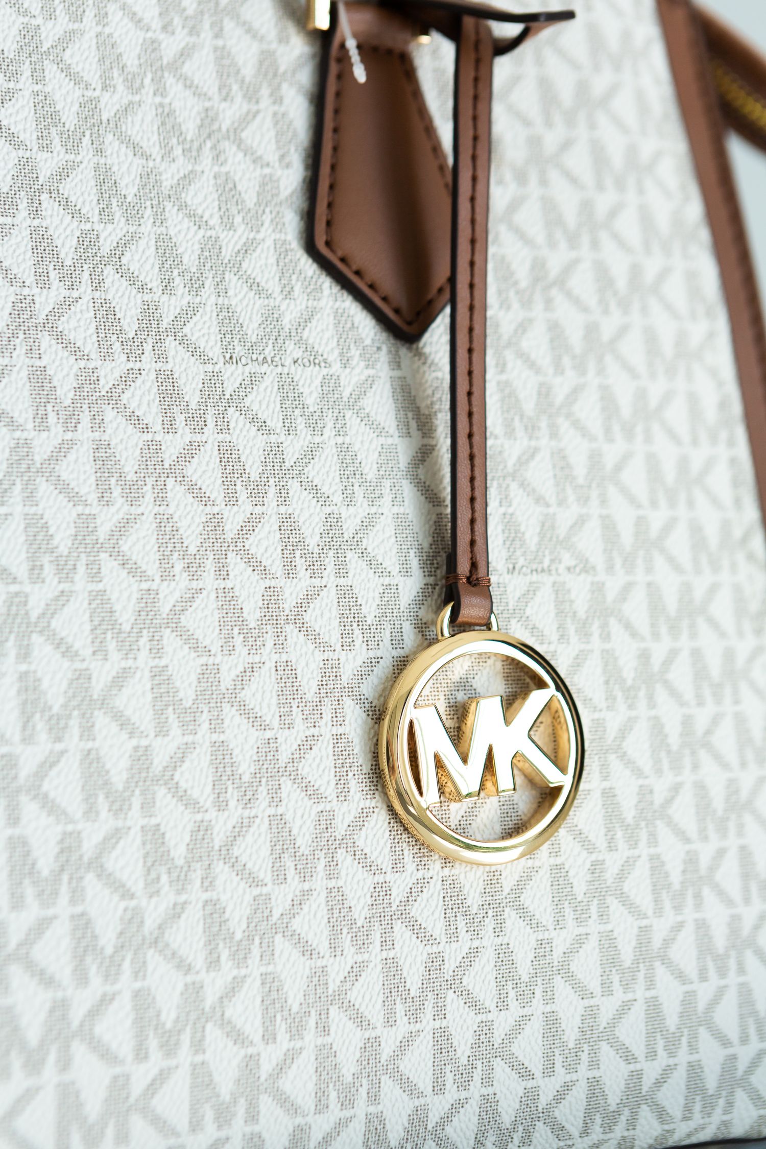 Close-up of Michael Kors logo charm on monogram patterned handbag.