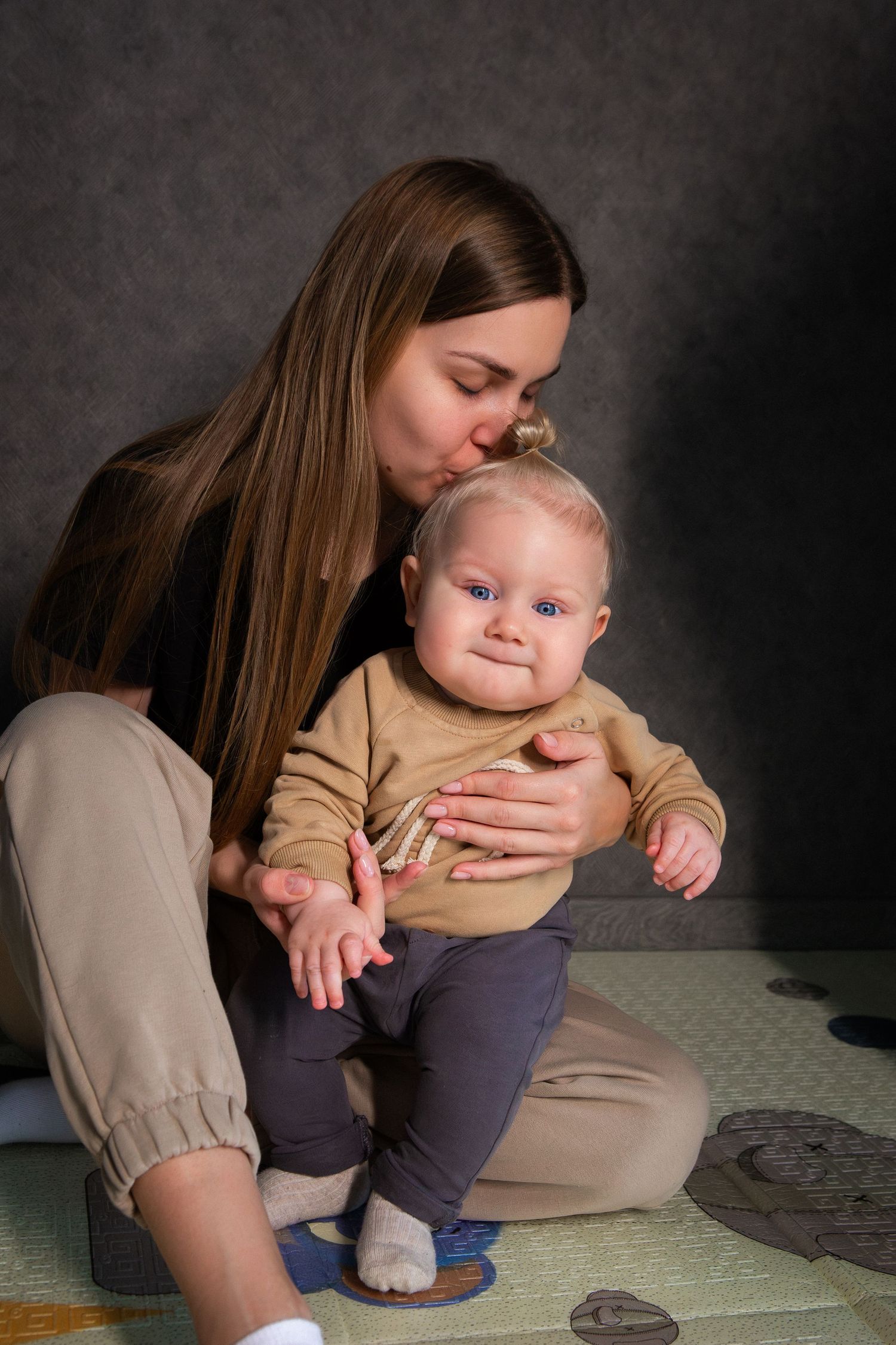 A parent in beige clothing shares tender moments with a baby wearing gray pants in a series of intimate portraits.