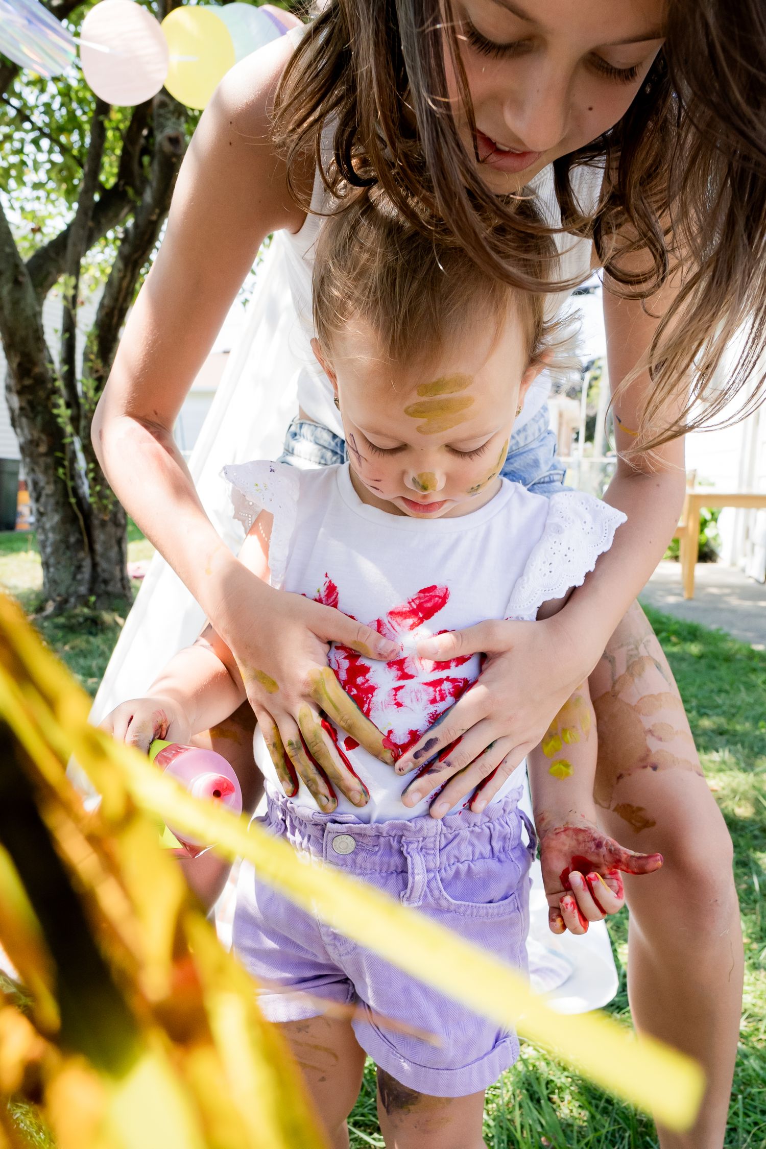 Paint-covered hands creating art together in a sunny garden setting.