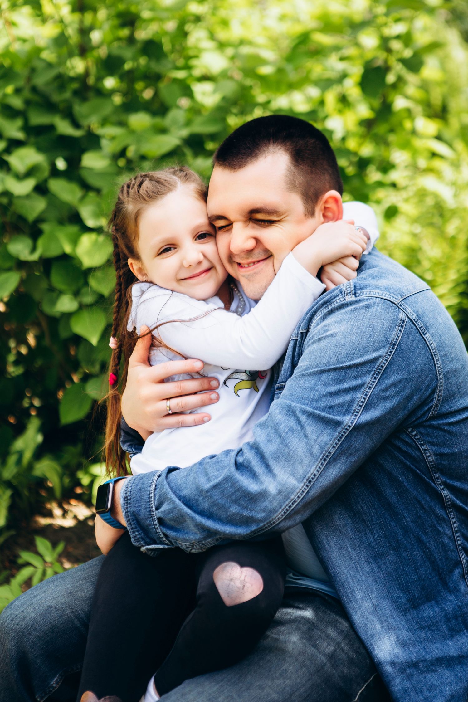 A tender embrace shared outdoors against a lush green garden backdrop.
