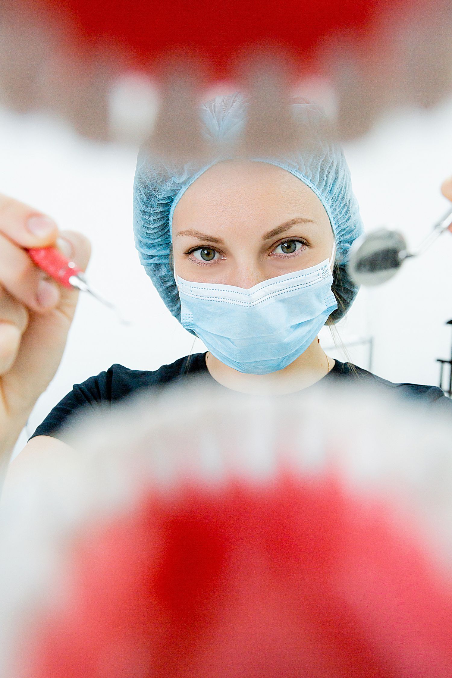 Healthcare professional wearing surgical mask and cap viewed through dental mirror reflection.