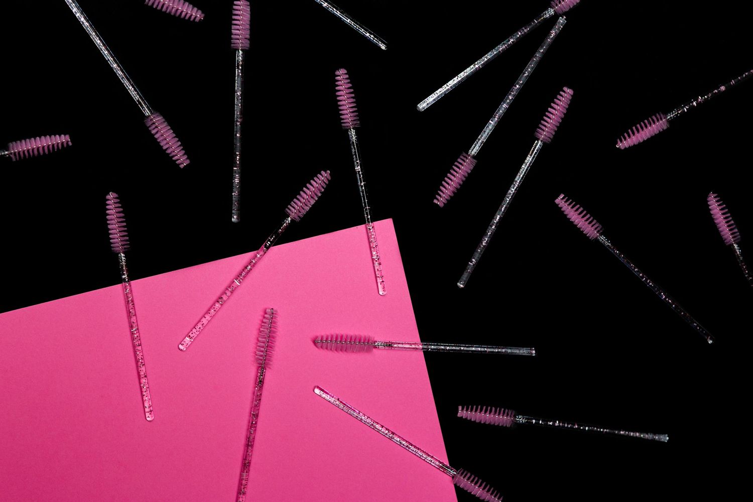 Pink dental brushes scattered on a black background with a pink surface edge.