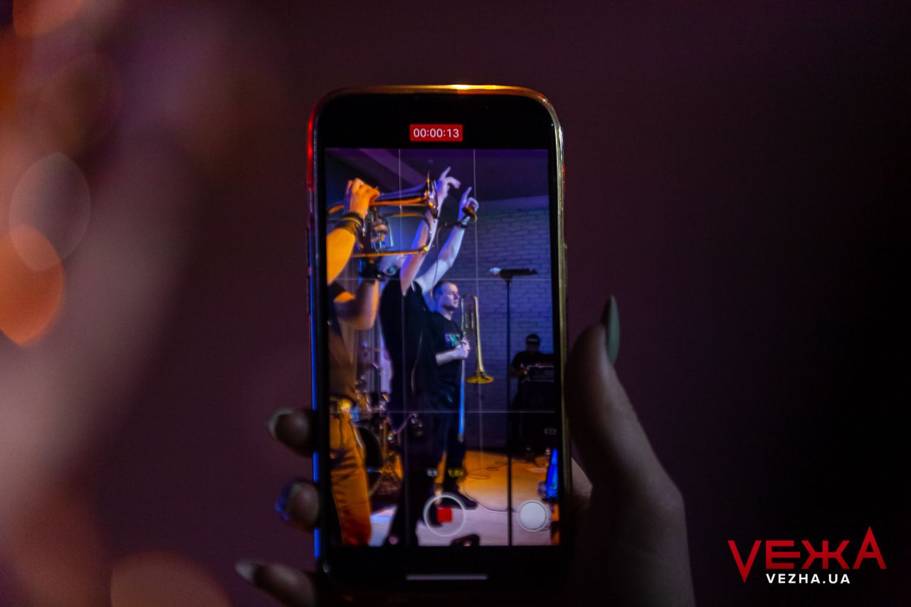 Phone screen captures live concert performance in dimly lit venue.