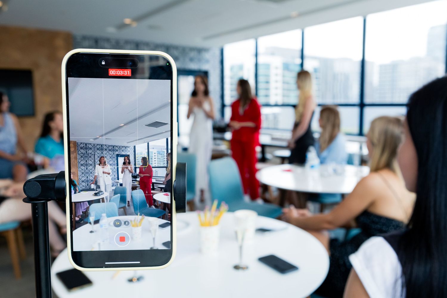 Phone screen capturing photo of gathering in modern office space with city views.