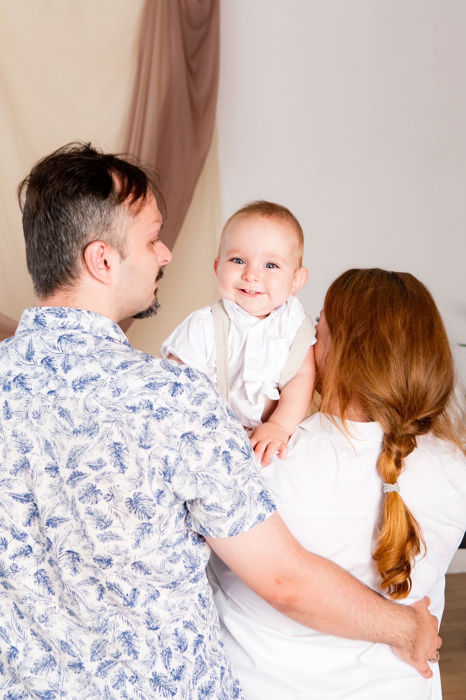 Happy family moment with parents holding smiling baby in white outfit.