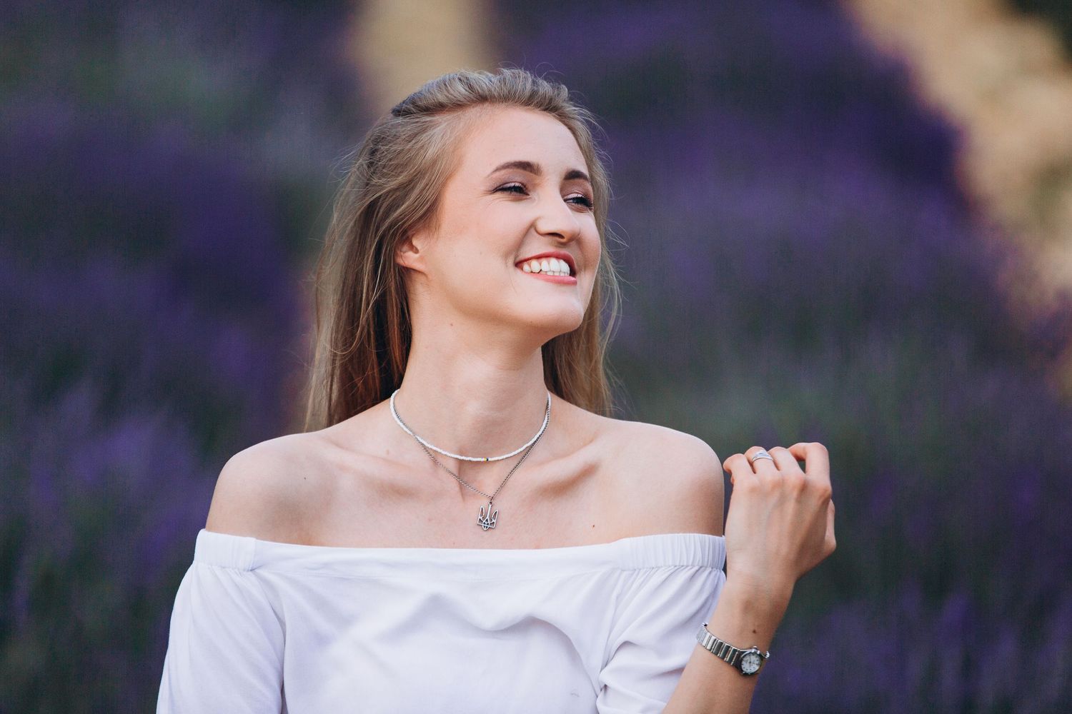Woman in white off-shoulder top posing in blooming lavender field.