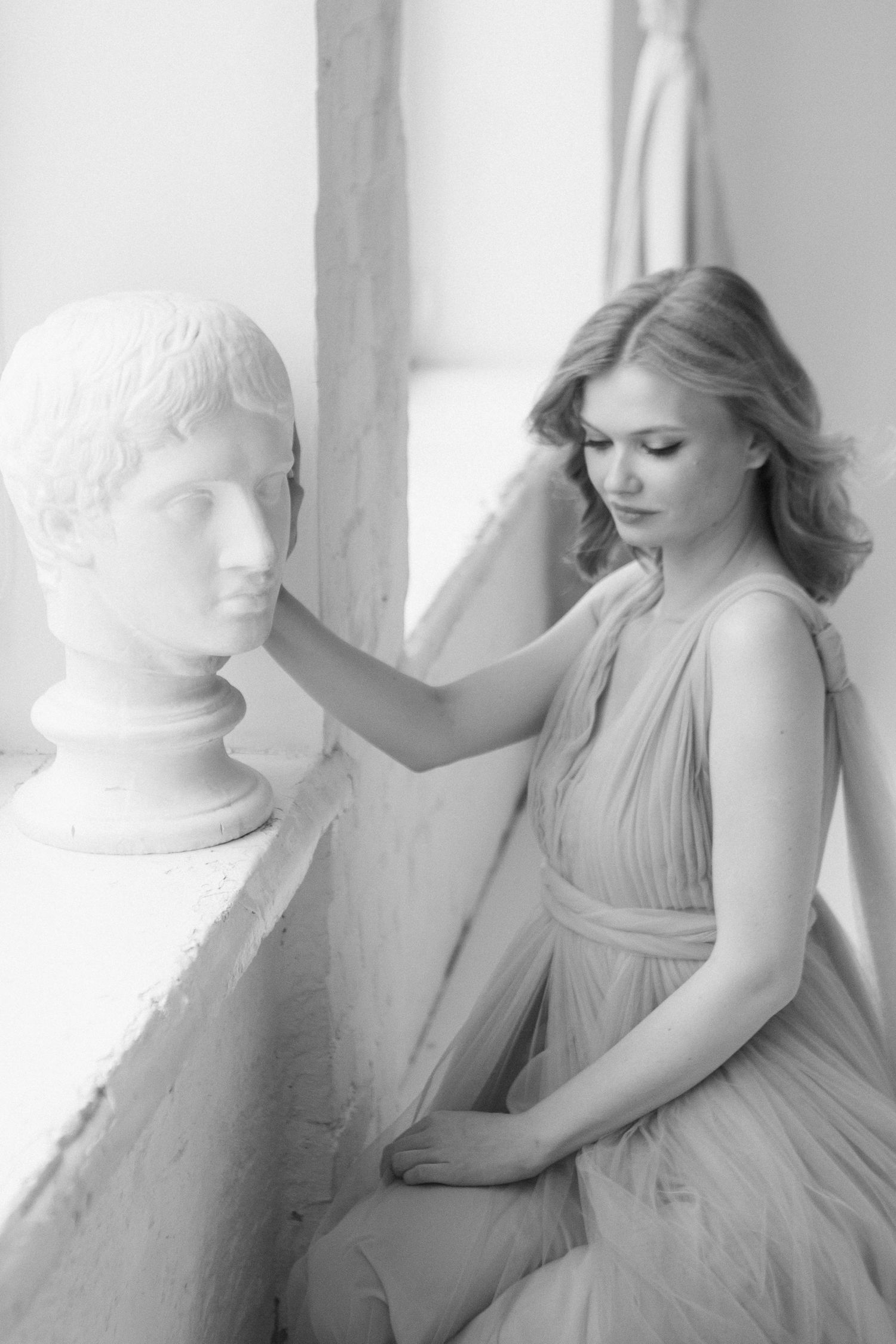 Dreamy black and white portrait with classical bust sculpture and flowing dress.