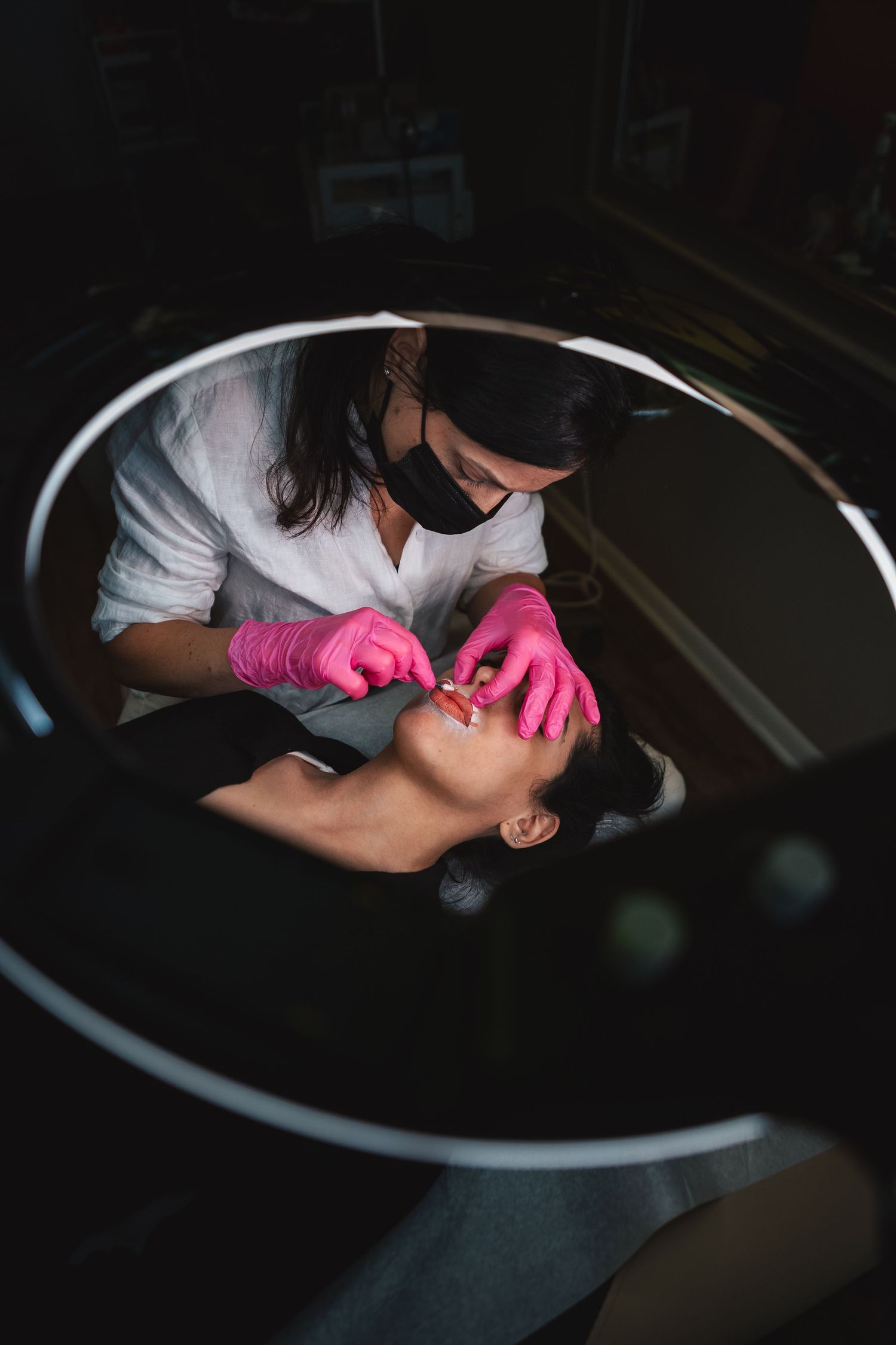 A dental professional wearing pink gloves performs a dental procedure in a dimly lit treatment room.