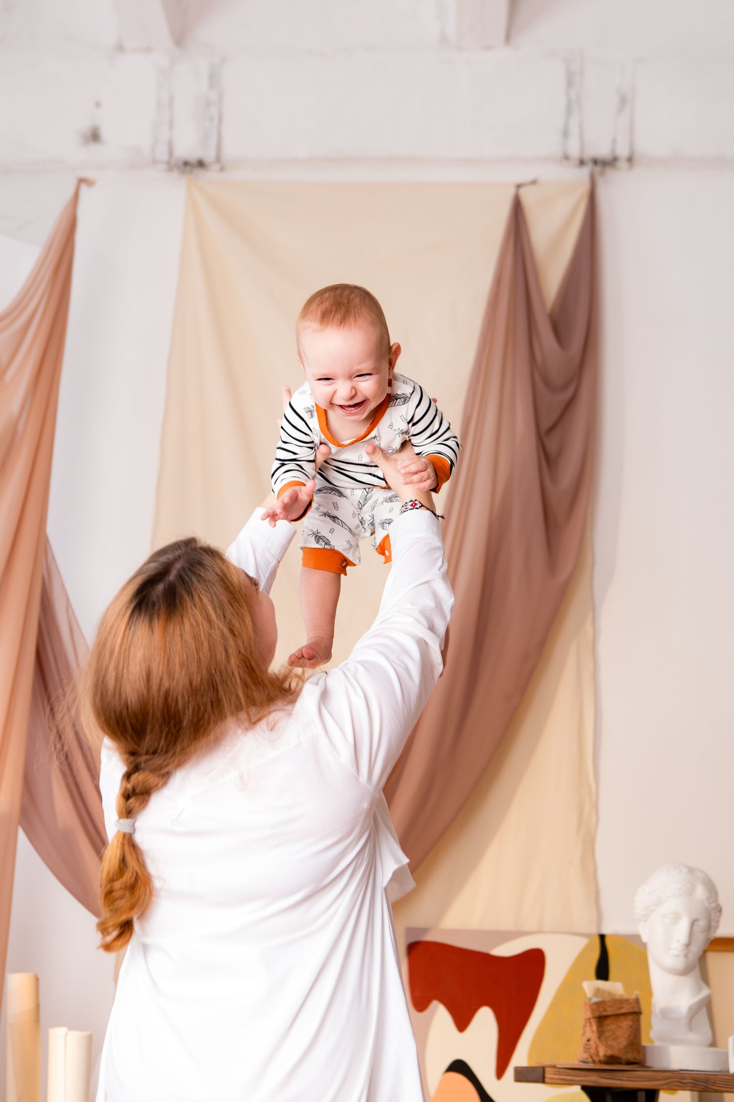 A joyful moment as a baby in stripes is lifted high in the air against draped fabric backdrops.