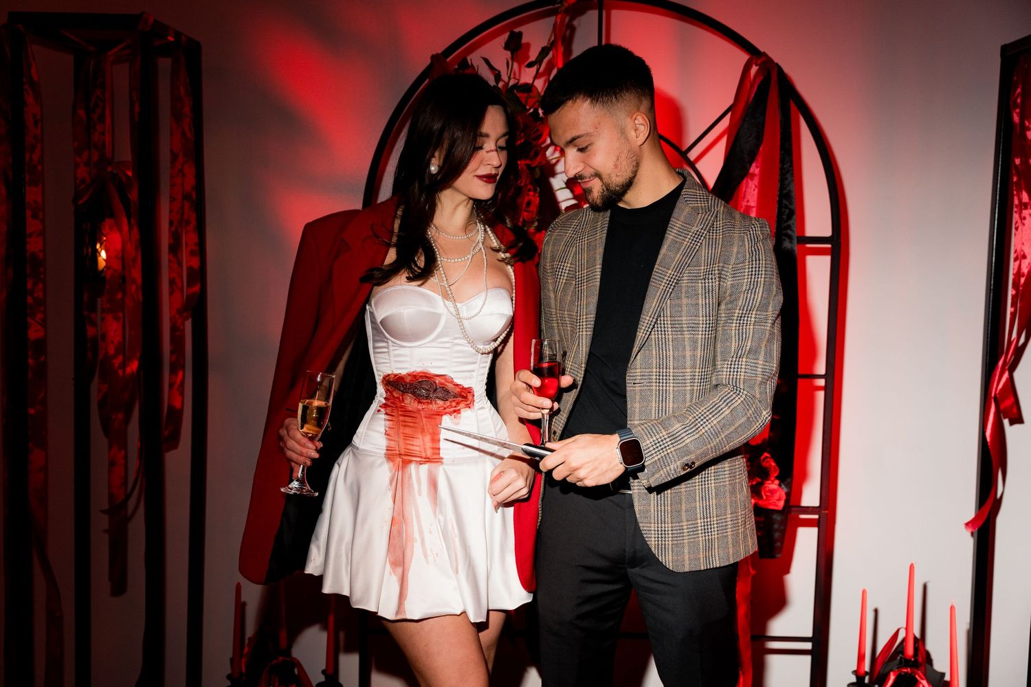 A couple poses together at a Halloween party under red lighting and gothic decorations.