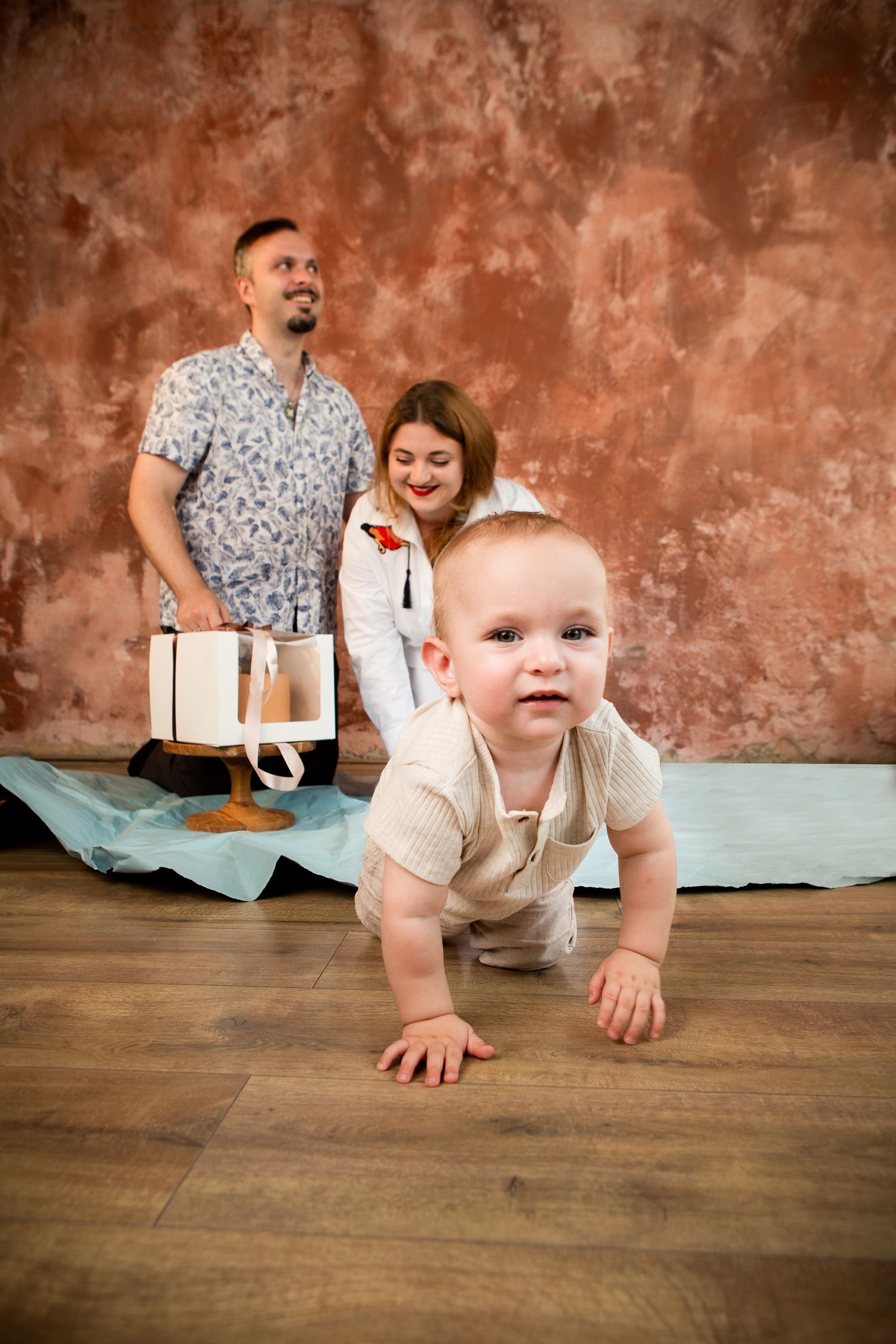 Baby crawling on wooden floor during family photo shoot with rustic background.