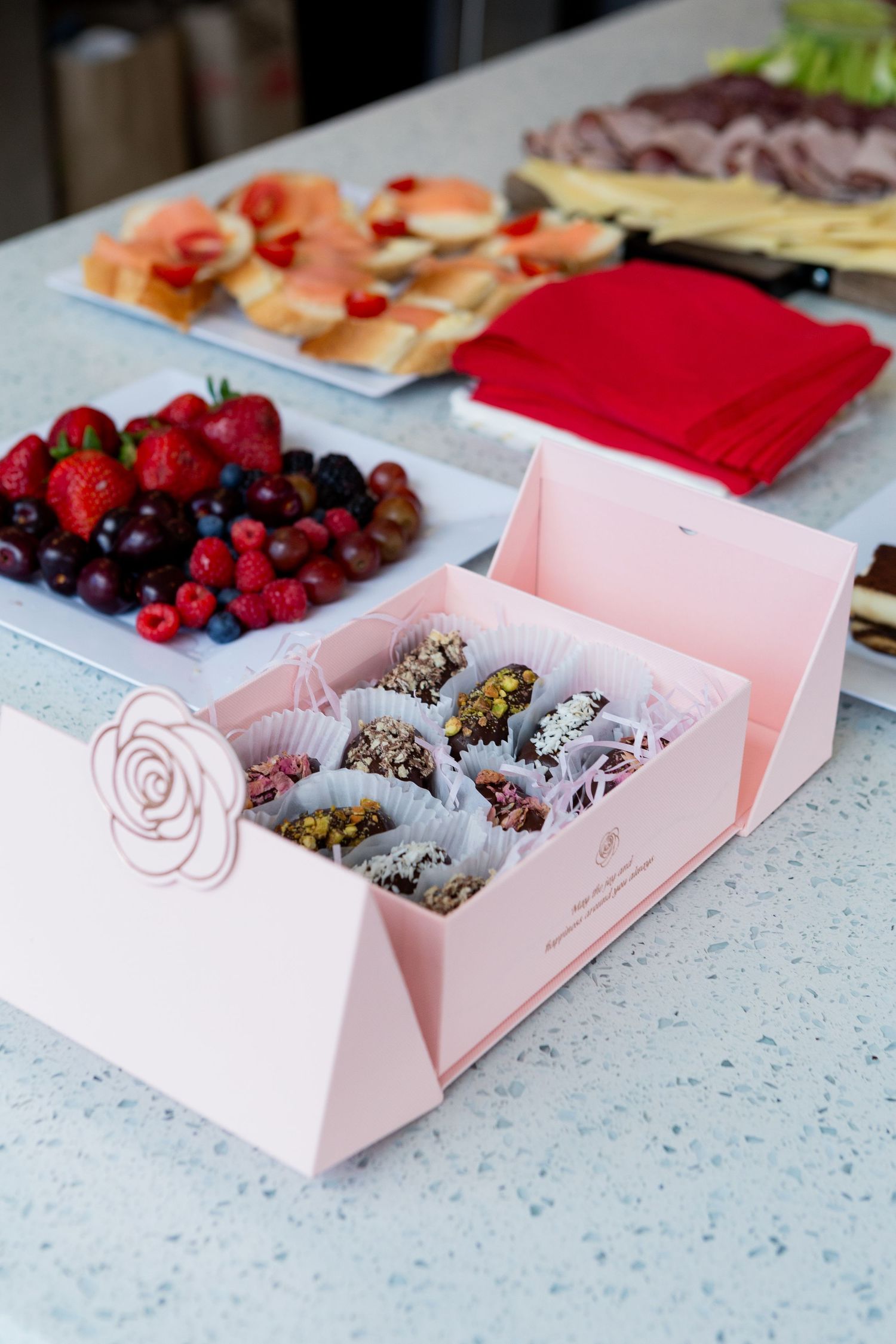 Pink box filled with decorated truffles alongside fresh berries on counter.