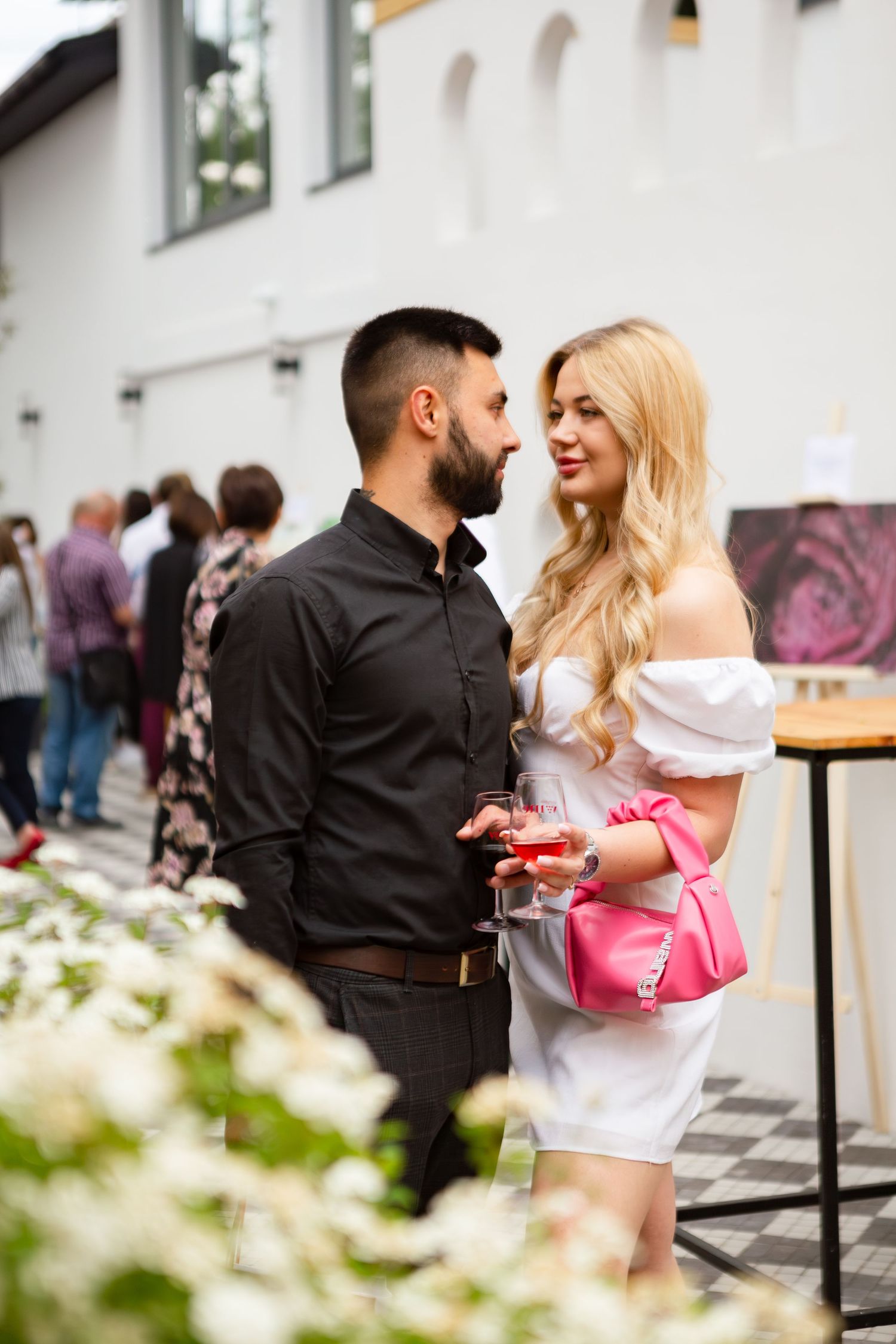 Couple enjoying drinks at an outdoor event venue with decorative flowers.