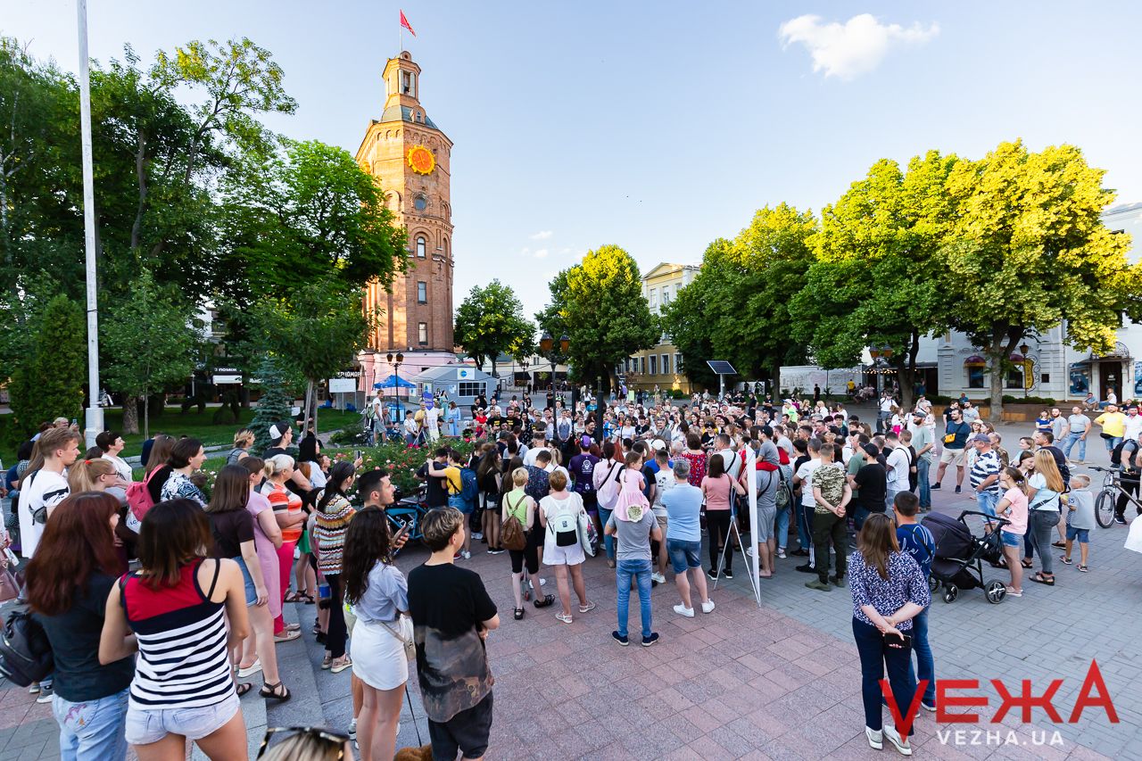 Large crowd gathered in a city square with a historic clock tower visible in the background.