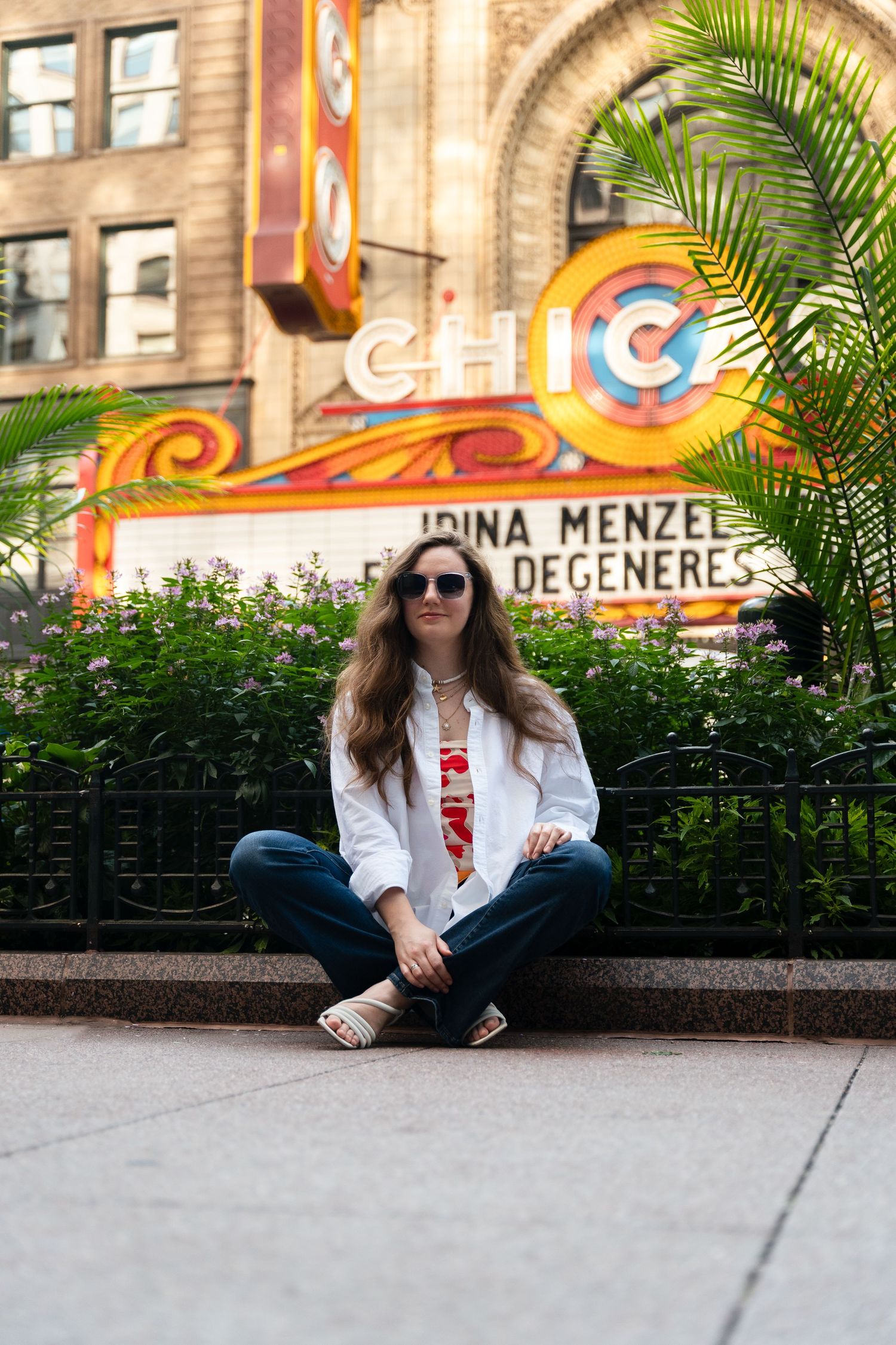 Casual portrait sitting in front of colorful Chicago Theater sign with palm frond in foreground.
