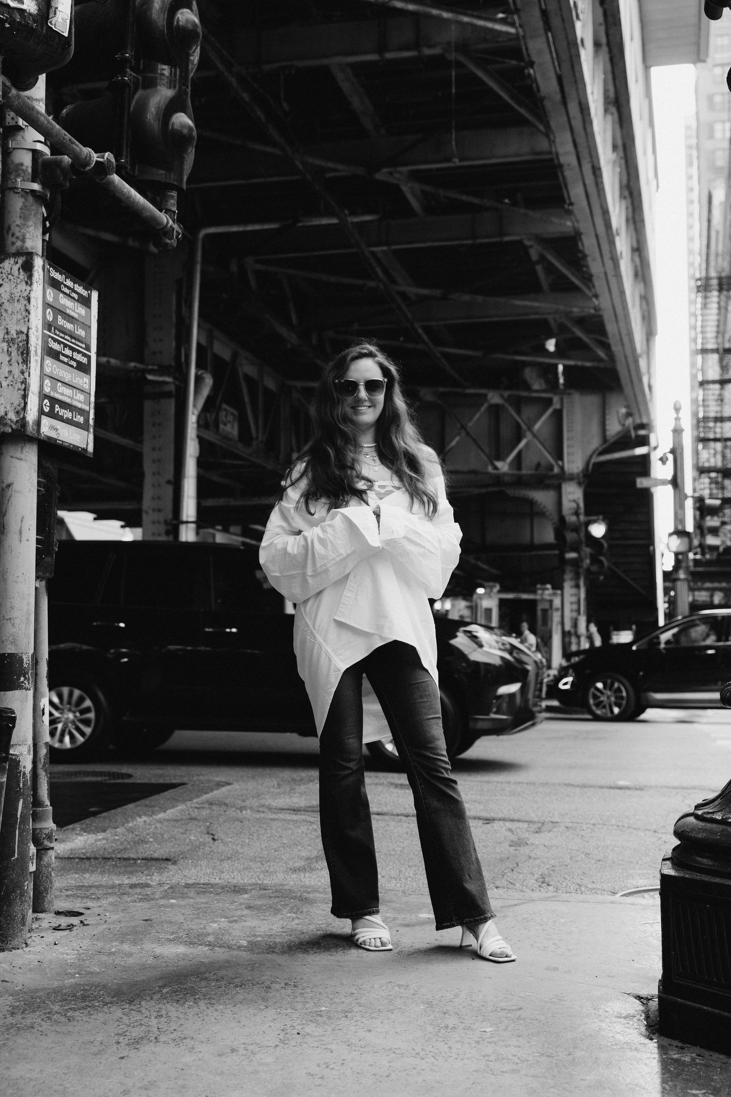 Black and white street fashion photo under elevated train tracks in urban setting.
