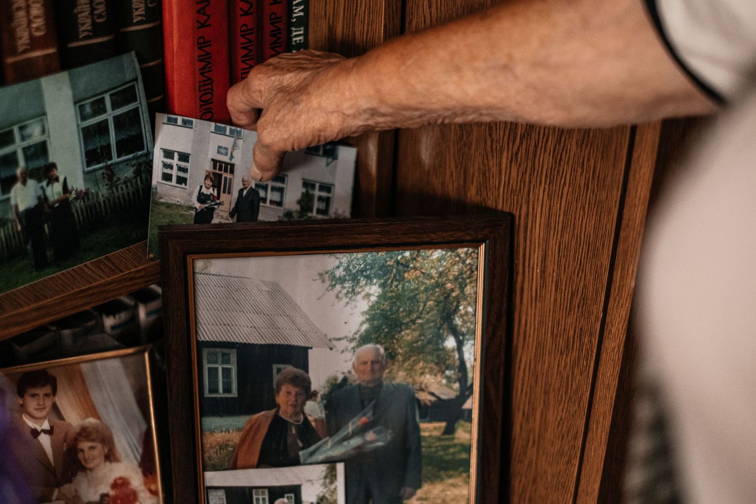 Hand holding an old photograph frame against a wooden surface with other photos visible.