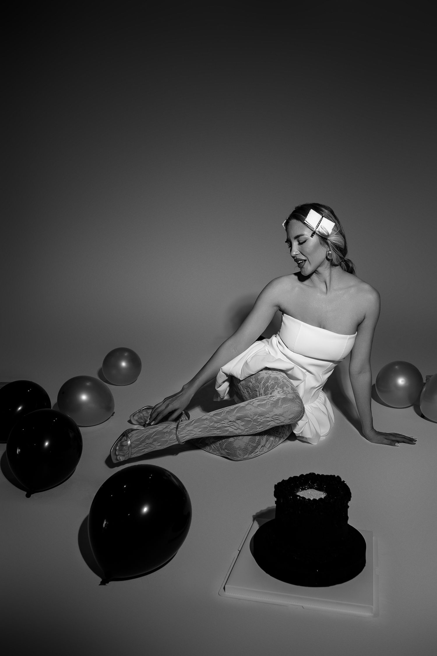 A dramatic black and white artistic photo series showing a figure in white posing with large black balloons on a light surface.
