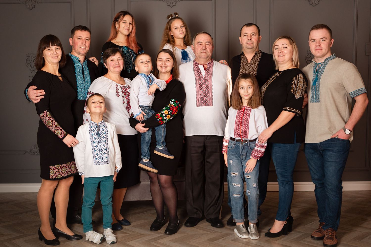 Extended family gathering wearing mix of traditional and modern clothing against gray backdrop.
