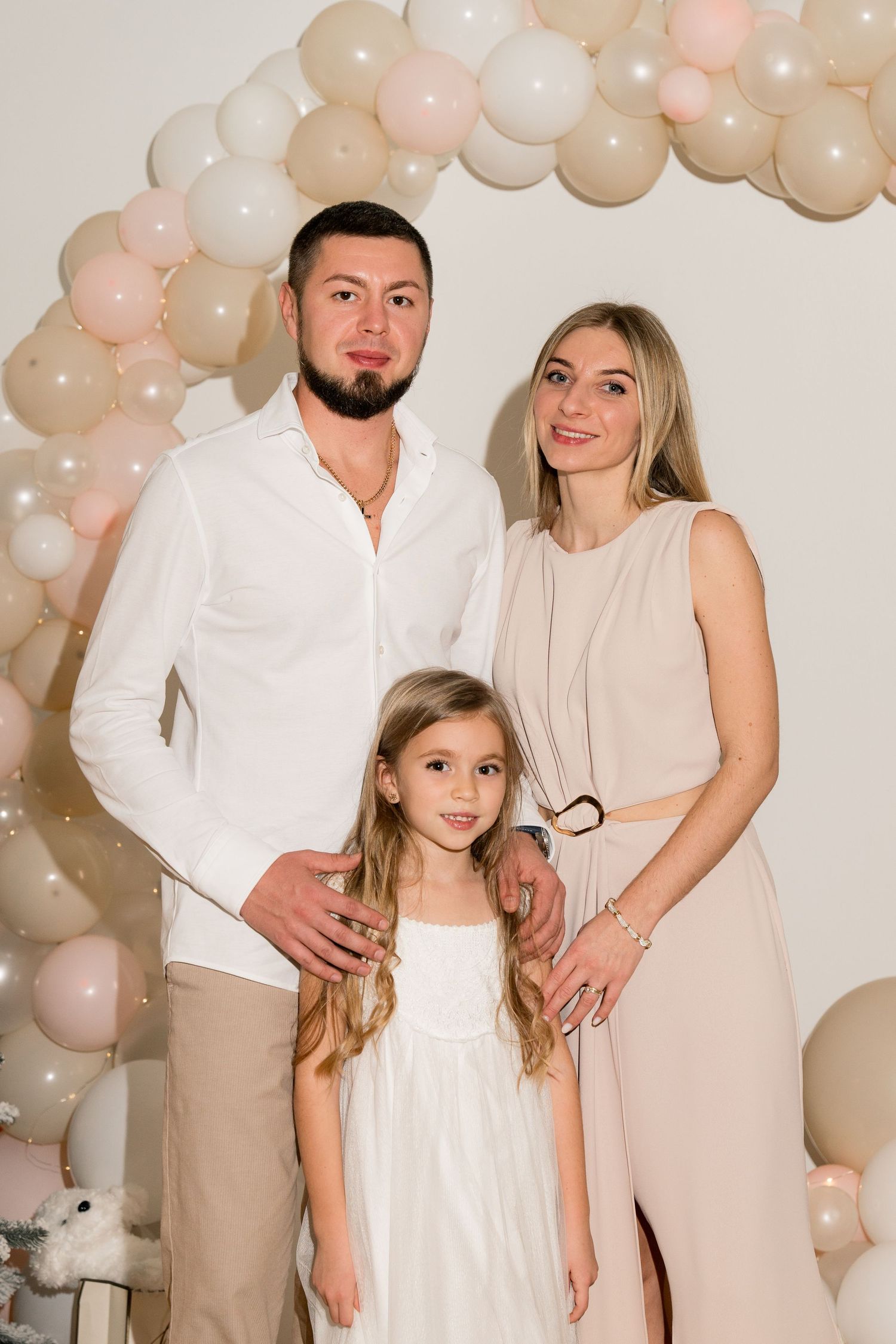 Family portrait with balloon arch backdrop in coordinated white and neutral outfits.