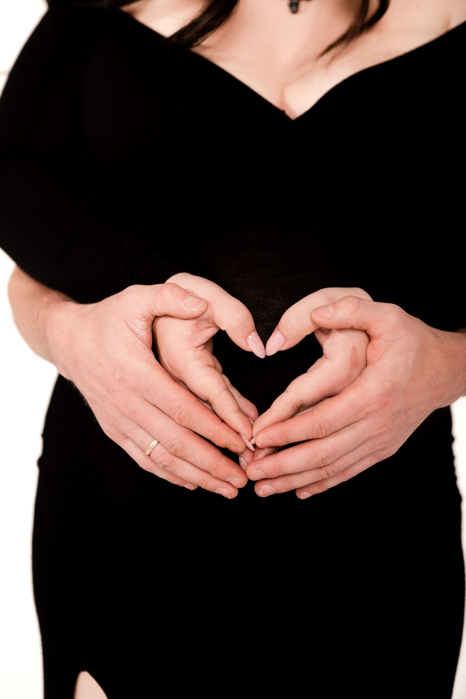 Hands forming heart shape over pregnant belly in black dress.