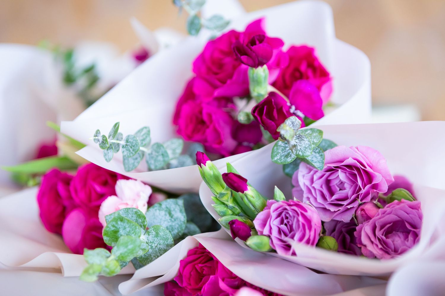 Vibrant pink and purple roses arranged in white bowls with delicate greenery.